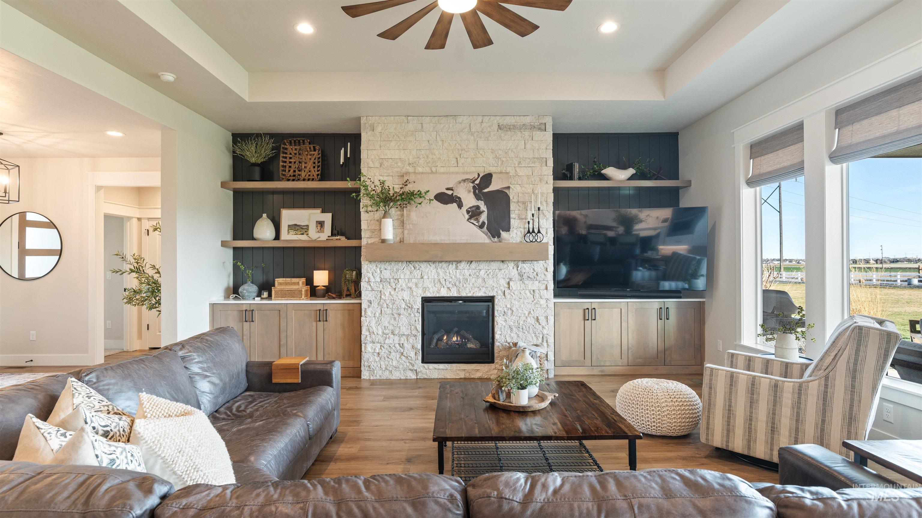 Living area featuring a tray ceiling, ceiling fan, wood finished floors, a stone fireplace, and recessed lighting