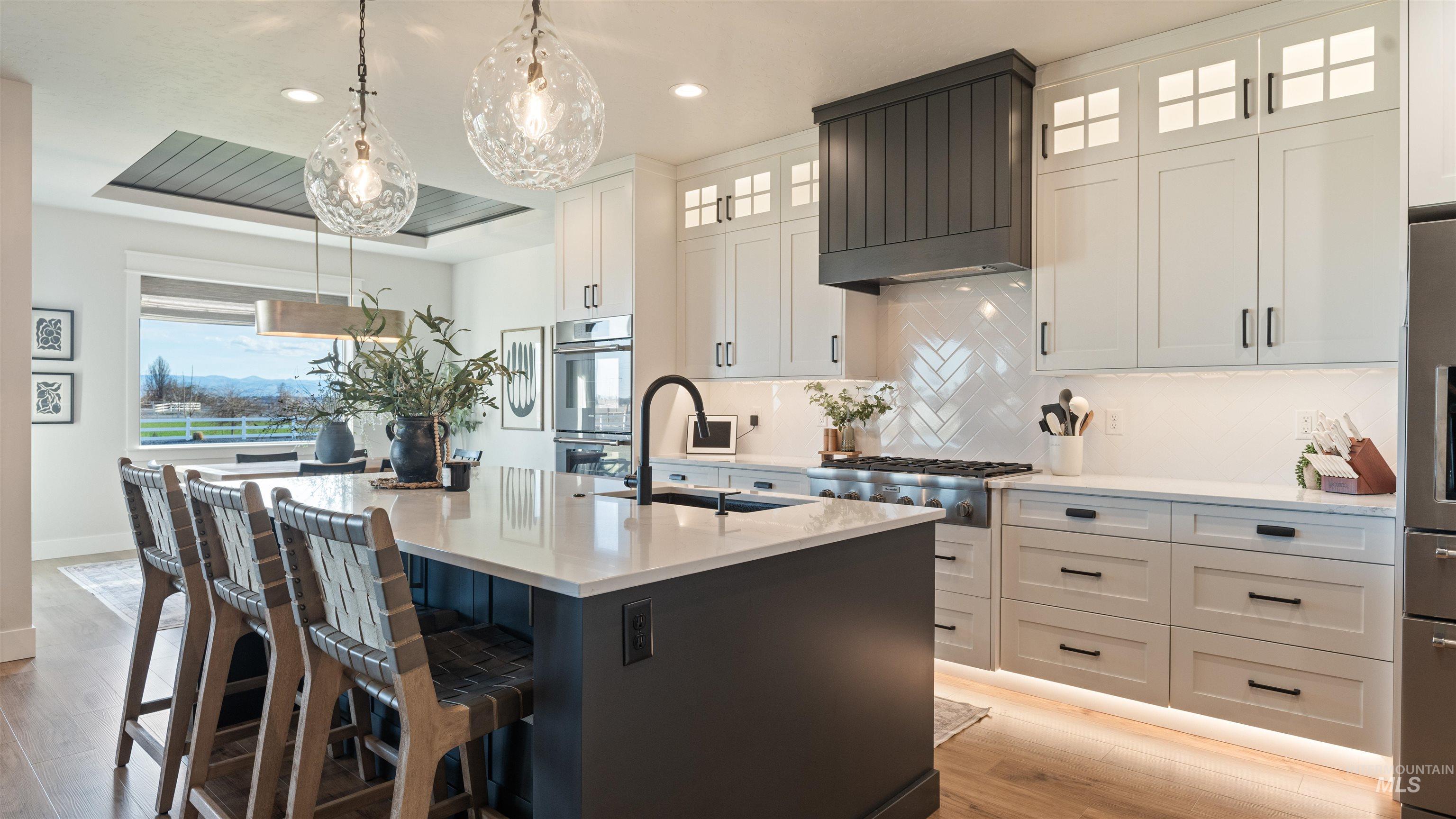 Dual tone kitchen featuring light wood-type flooring, two tone cabinets, backsplash, a center island with sink, and a kitchen bar
