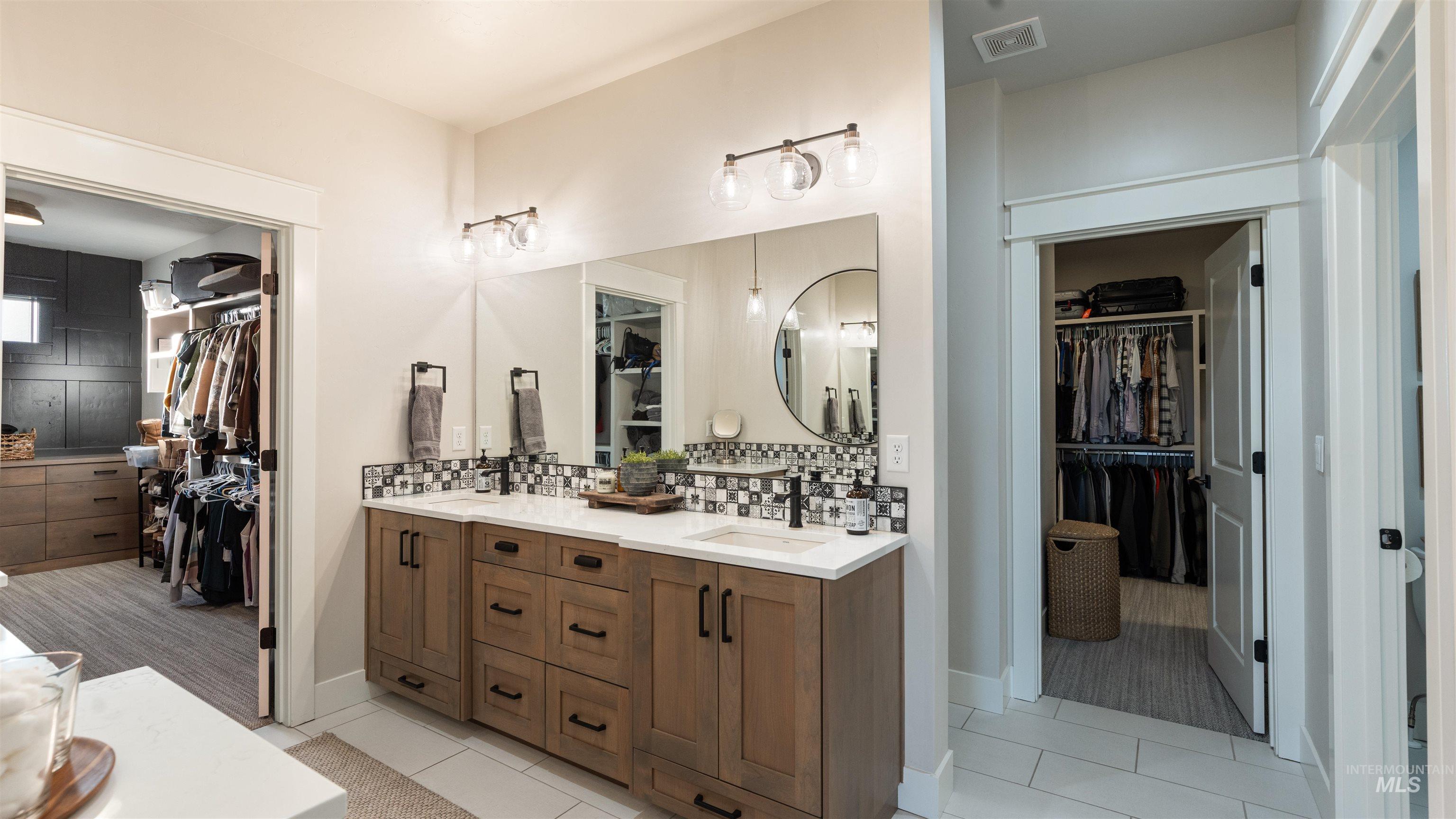 Full bath with a spacious closet, double vanity, light tile patterned floors, and decorative backsplash