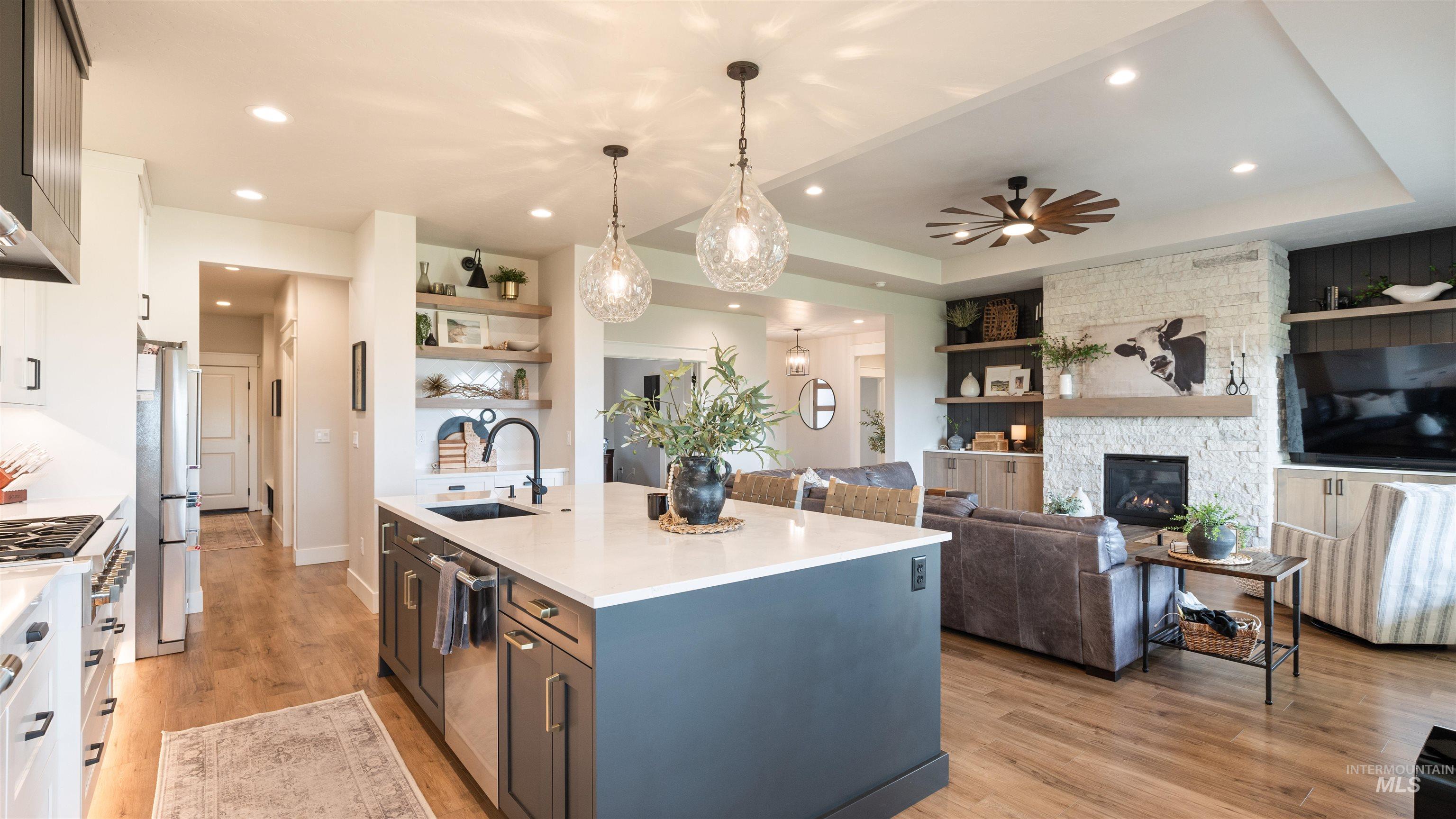 Kitchen featuring open floor plan, light wood-type flooring, an island with sink, decorative light fixtures, and light stone counters