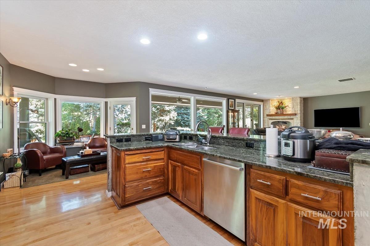 Kitchen with open floor plan, brown cabinets, dishwasher, dark stone counters, and recessed lighting