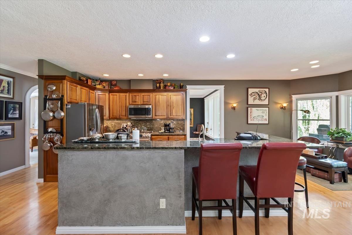 Kitchen with light wood finished floors, arched walkways, decorative backsplash, appliances with stainless steel finishes, and brown cabinetry