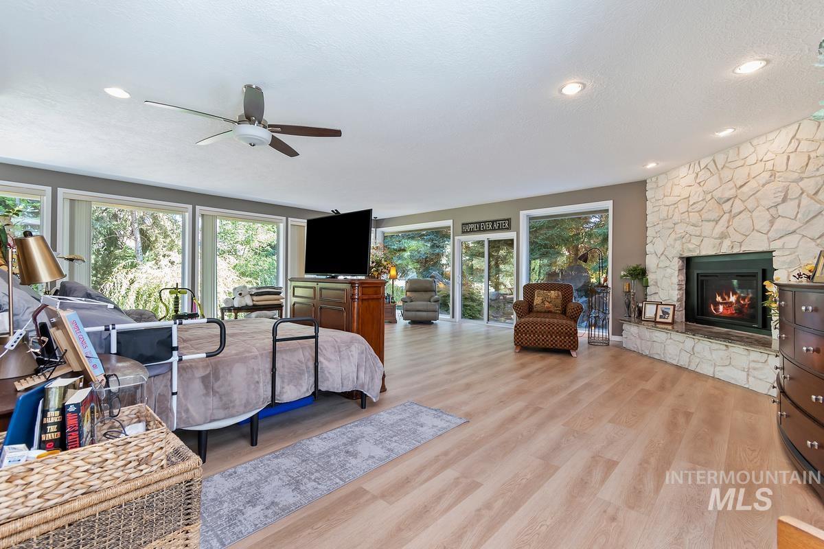 Bedroom featuring a stone fireplace, light wood-style floors, a textured ceiling, recessed lighting, and a ceiling fan