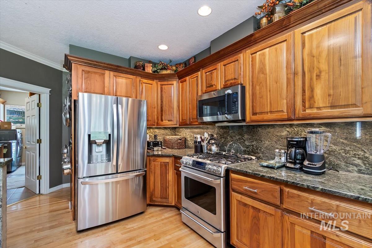 Kitchen featuring stainless steel appliances, dark stone countertops, brown cabinetry, a textured ceiling, and crown molding
