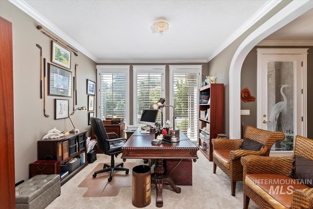 Home office with light colored carpet, crown molding, arched walkways, and a textured ceiling