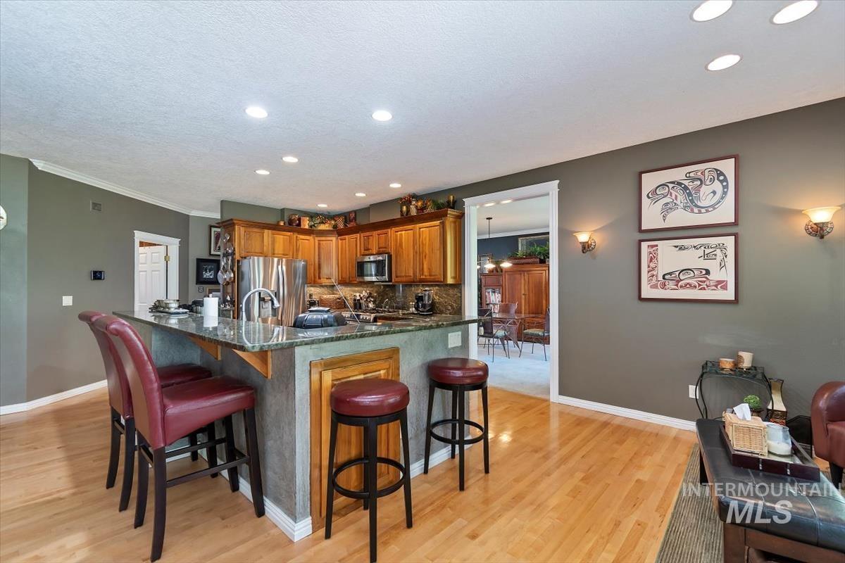 Kitchen featuring brown cabinets, a breakfast bar, backsplash, dark stone countertops, and light wood-style flooring