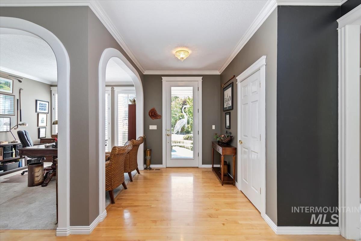 Foyer featuring crown molding, arched walkways, and light wood-type flooring