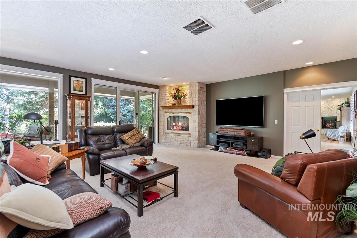 Carpeted living room with a stone fireplace, a textured ceiling, and recessed lighting