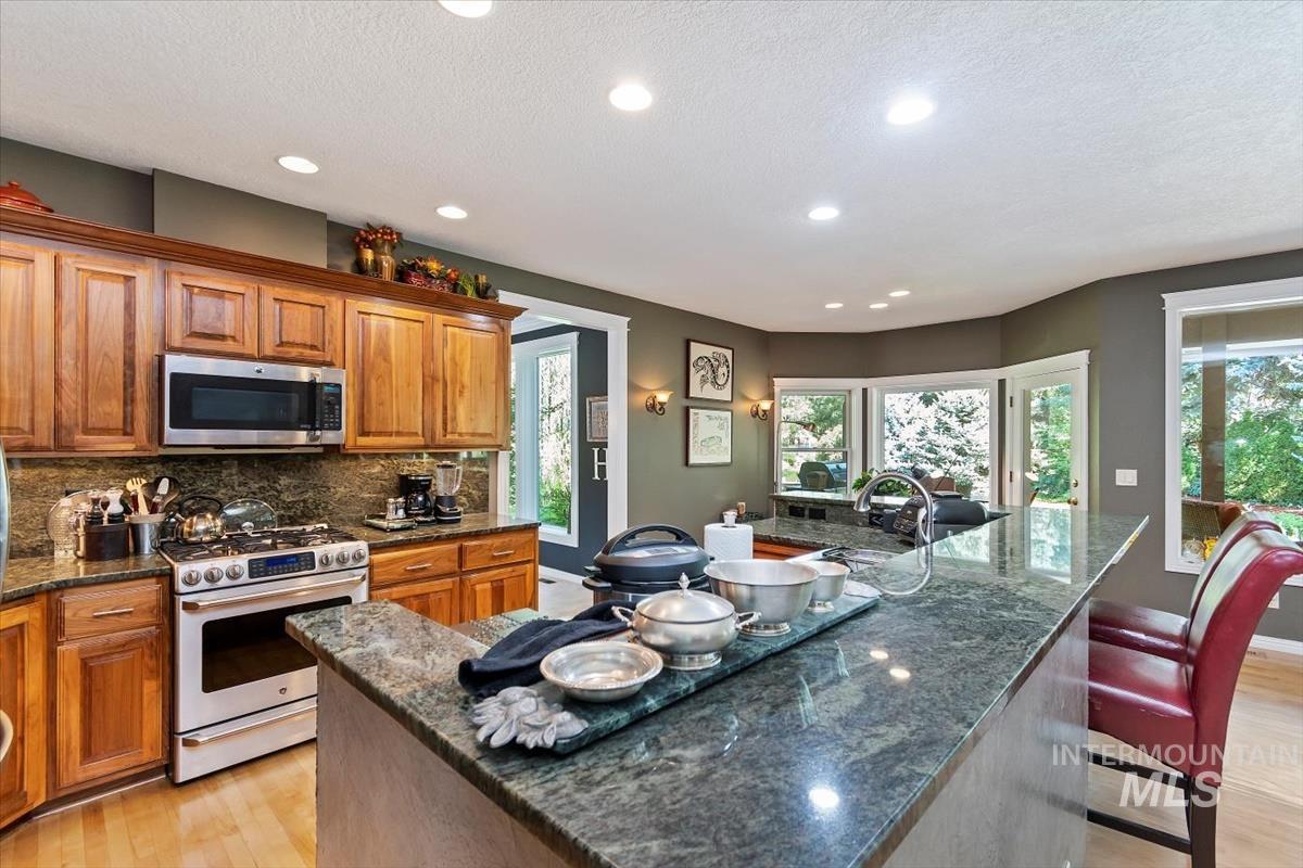 Kitchen featuring light wood-type flooring, brown cabinets, stainless steel appliances, dark stone counters, and recessed lighting