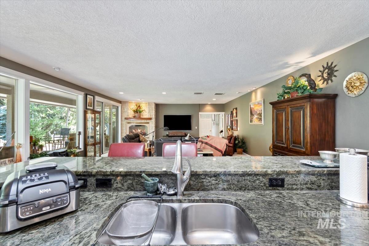 Kitchen featuring a fireplace, a textured ceiling, open floor plan, dark stone counters, and recessed lighting