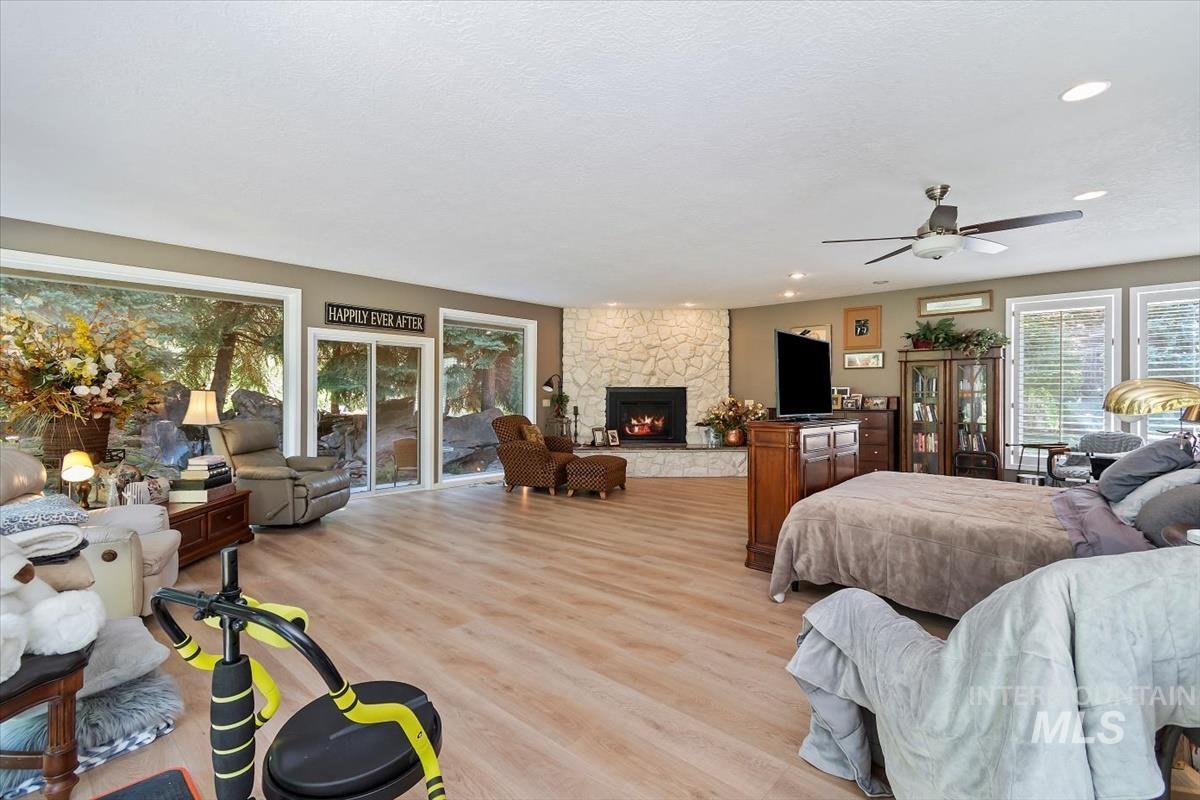 Bedroom featuring light wood finished floors, a stone fireplace, a ceiling fan, and access to exterior