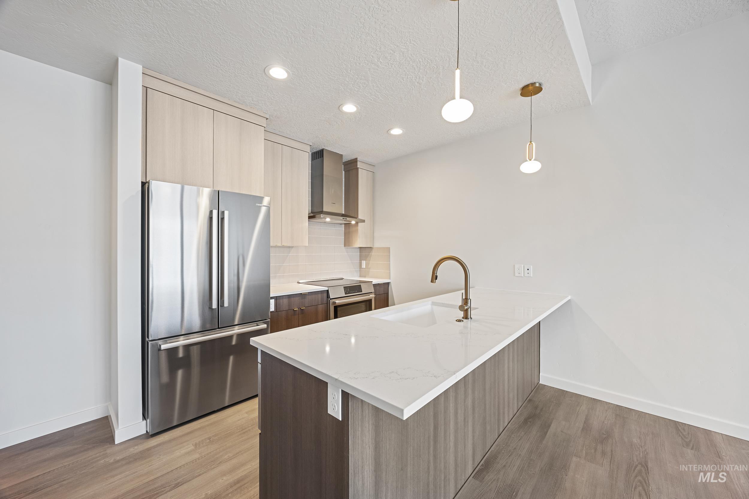 Kitchen with modern cabinets, stainless steel appliances, light stone counters, decorative light fixtures, and a textured ceiling