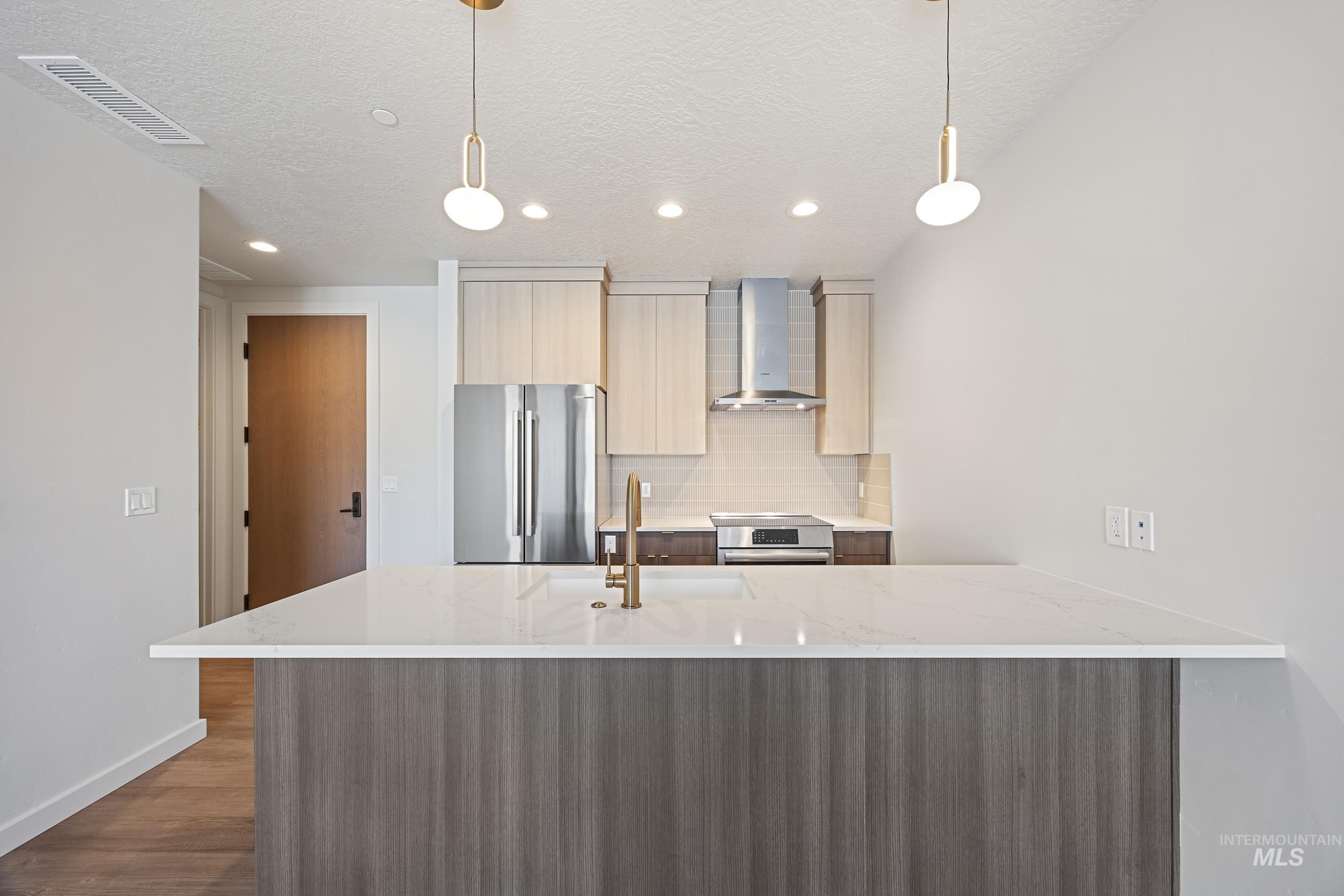 Kitchen featuring modern cabinets, light stone counters, backsplash, wall chimney exhaust hood, and a peninsula