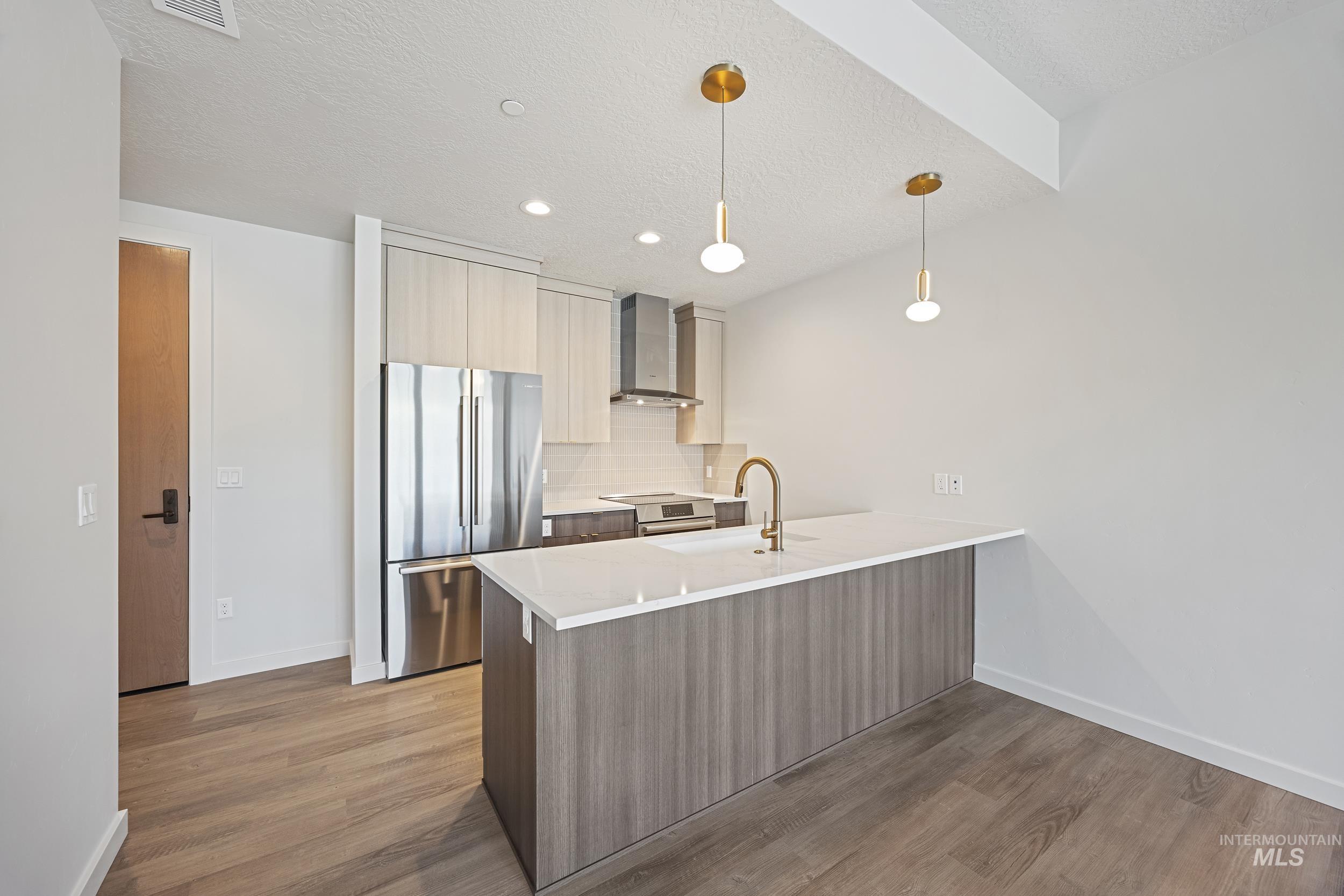 Kitchen featuring modern cabinets, appliances with stainless steel finishes, decorative light fixtures, a peninsula, and dark wood-type flooring
