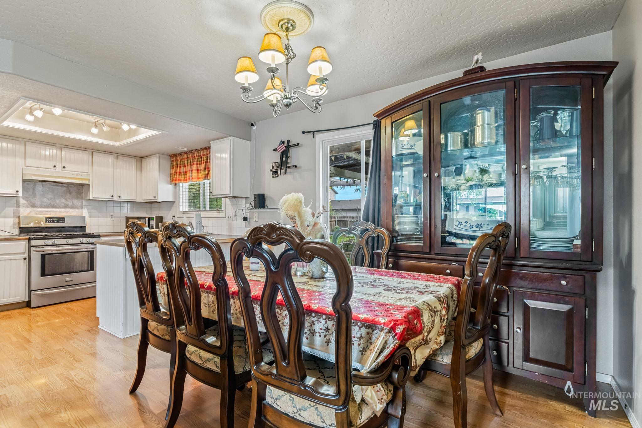 Dining area featuring a textured ceiling, a chandelier, light wood-style floors, and a raised ceiling