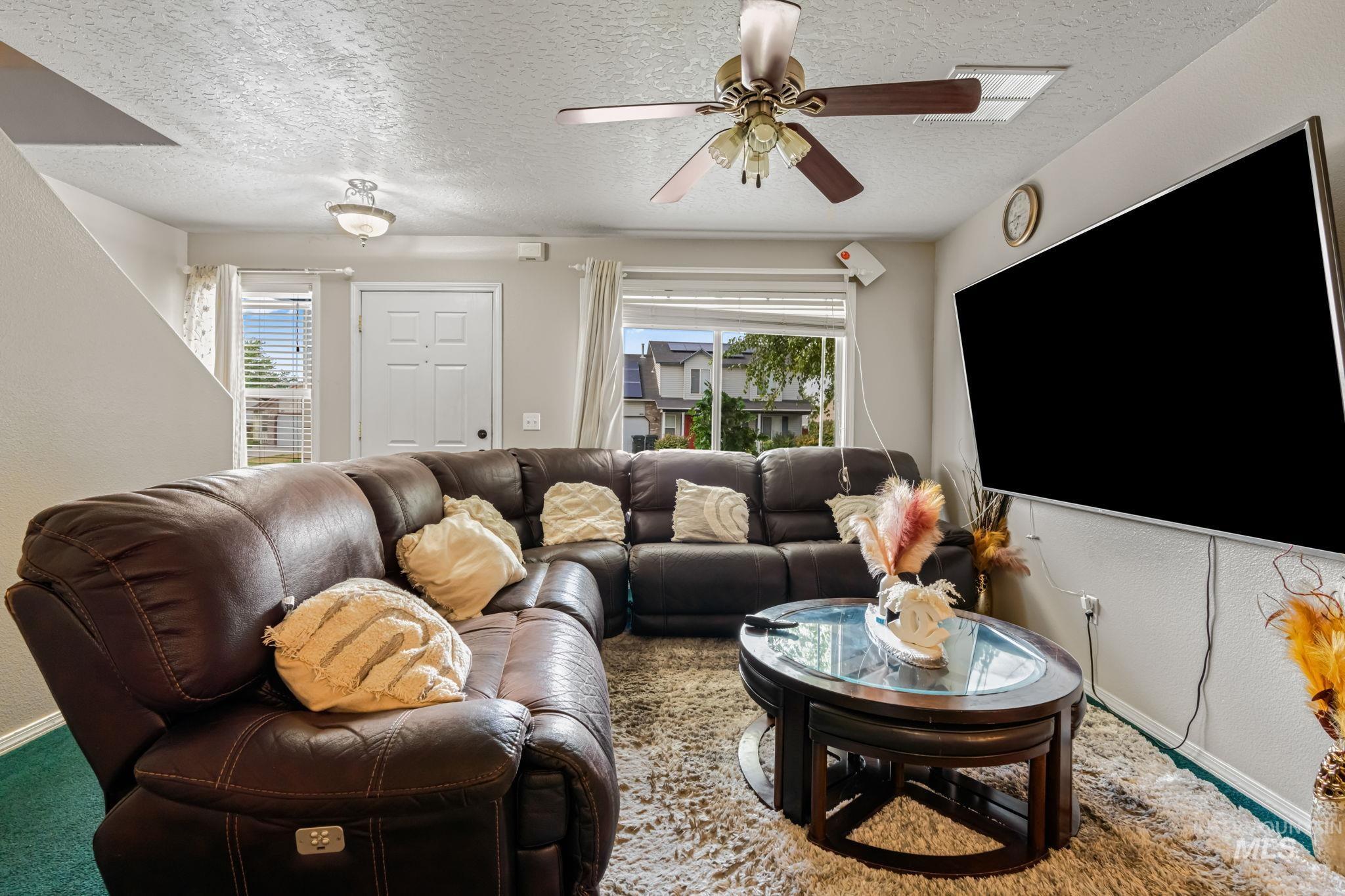 Carpeted living room with a textured ceiling, a textured wall, plenty of natural light, and a ceiling fan