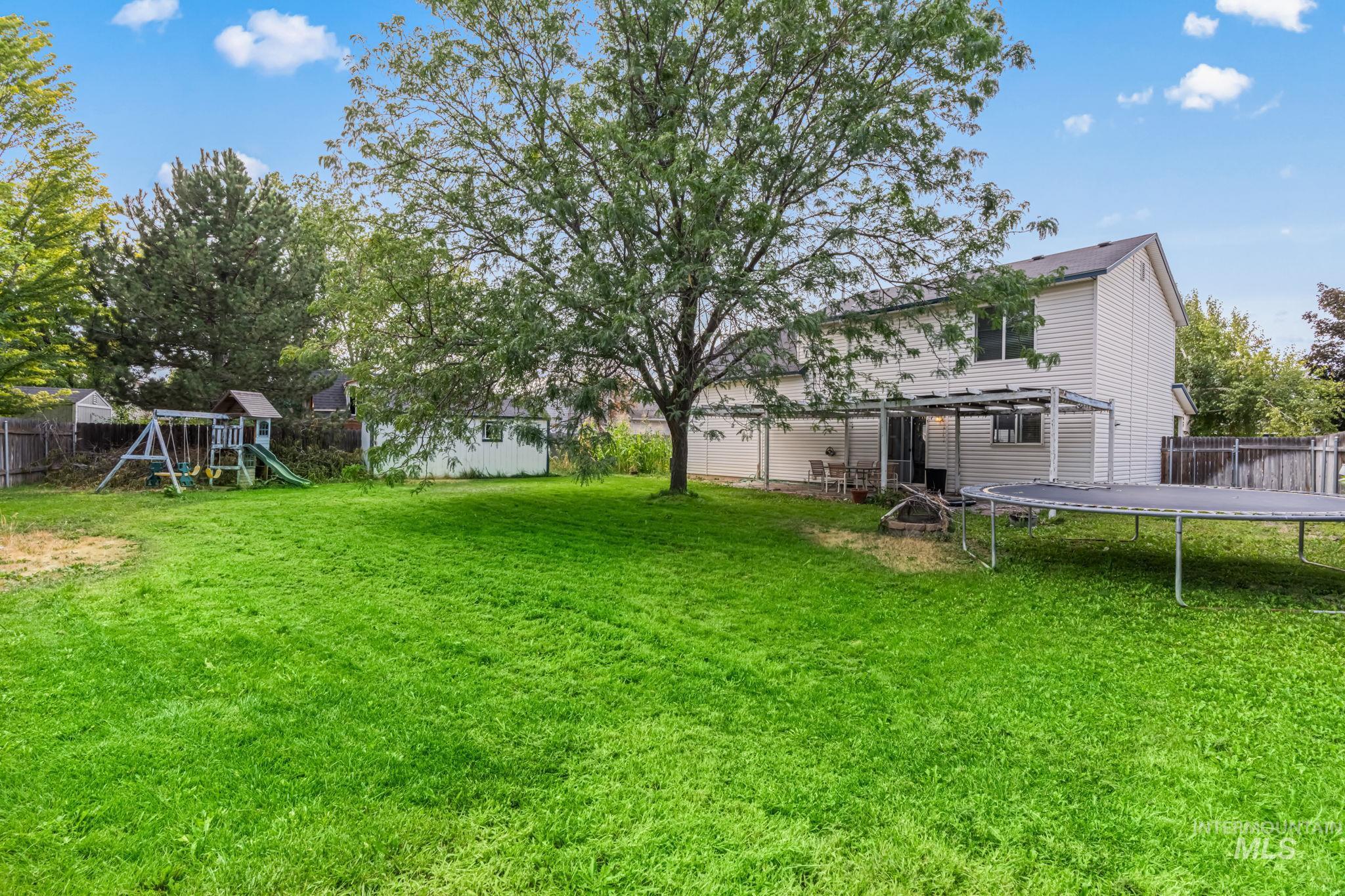 Fenced backyard featuring a trampoline and a playground