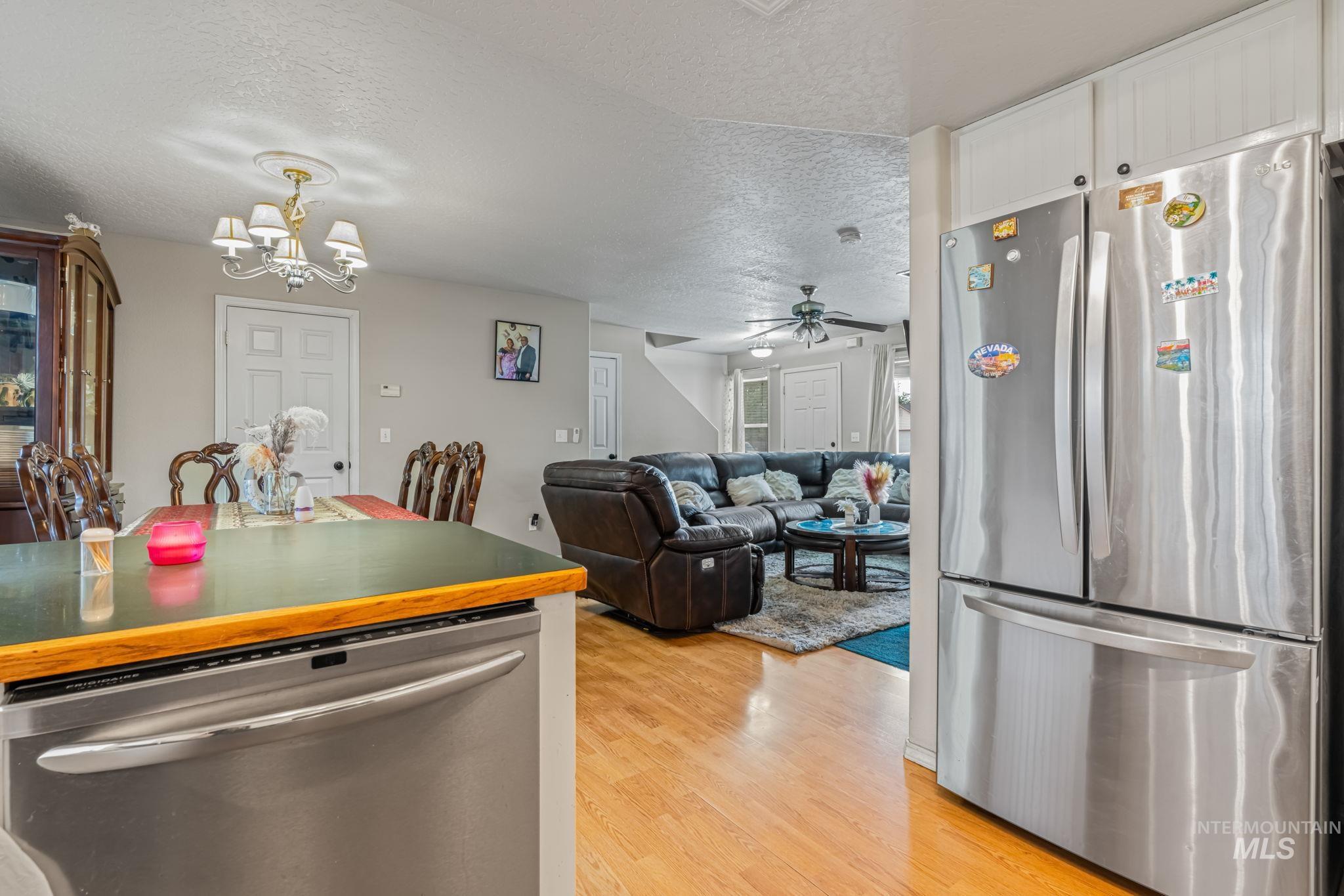 Kitchen with appliances with stainless steel finishes, a textured ceiling, light wood-type flooring, ceiling fan, and a chandelier