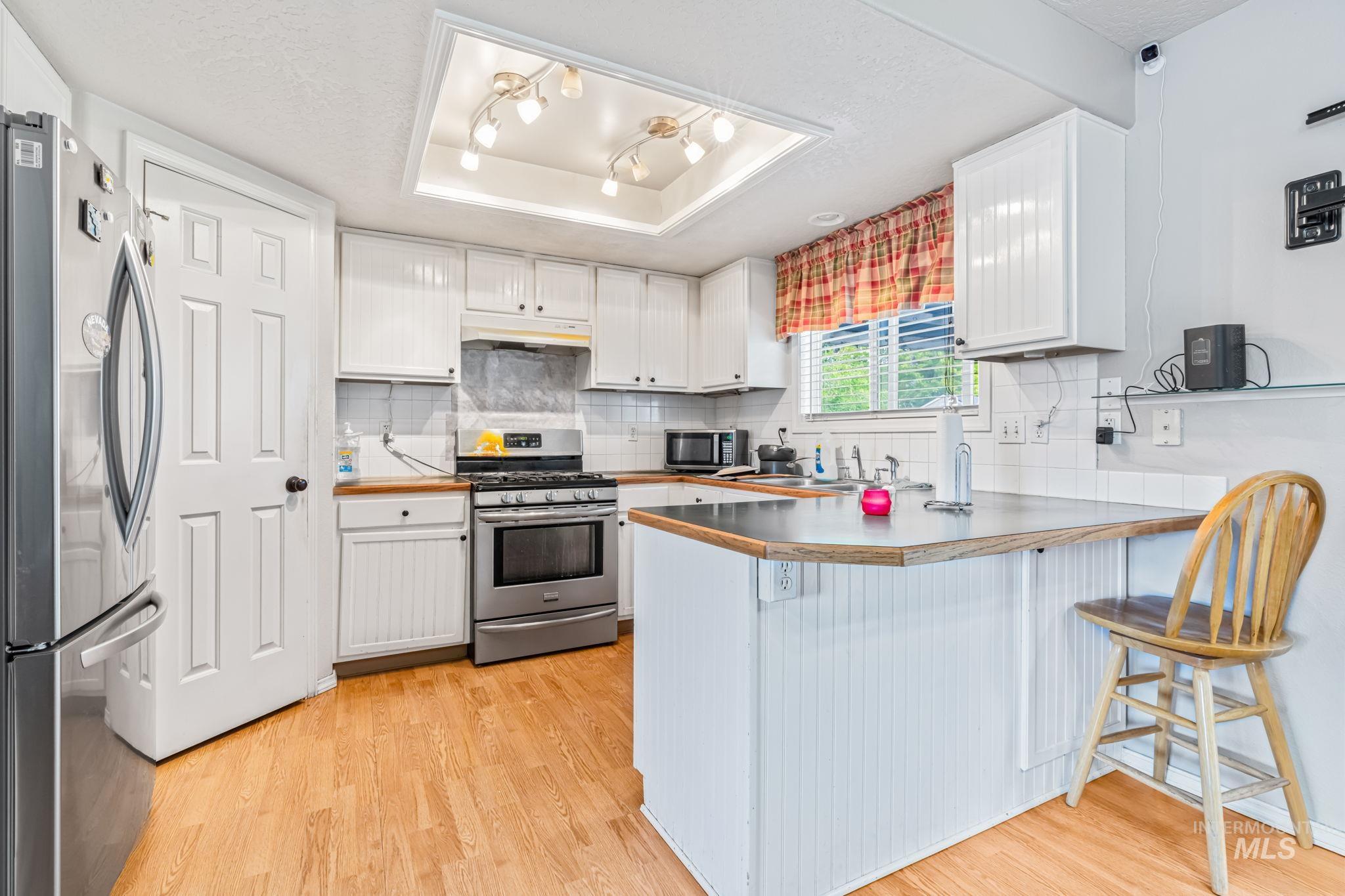 Kitchen featuring white cabinets, stainless steel appliances, a raised ceiling, backsplash, and light wood-style flooring