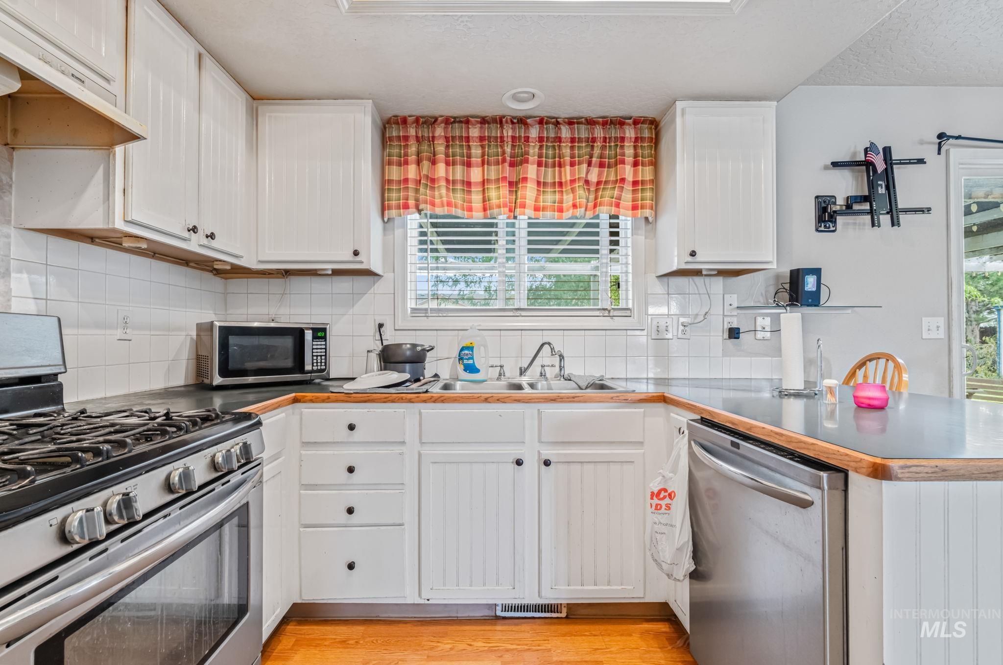 Kitchen with appliances with stainless steel finishes, plenty of natural light, decorative backsplash, white cabinetry, and a textured ceiling