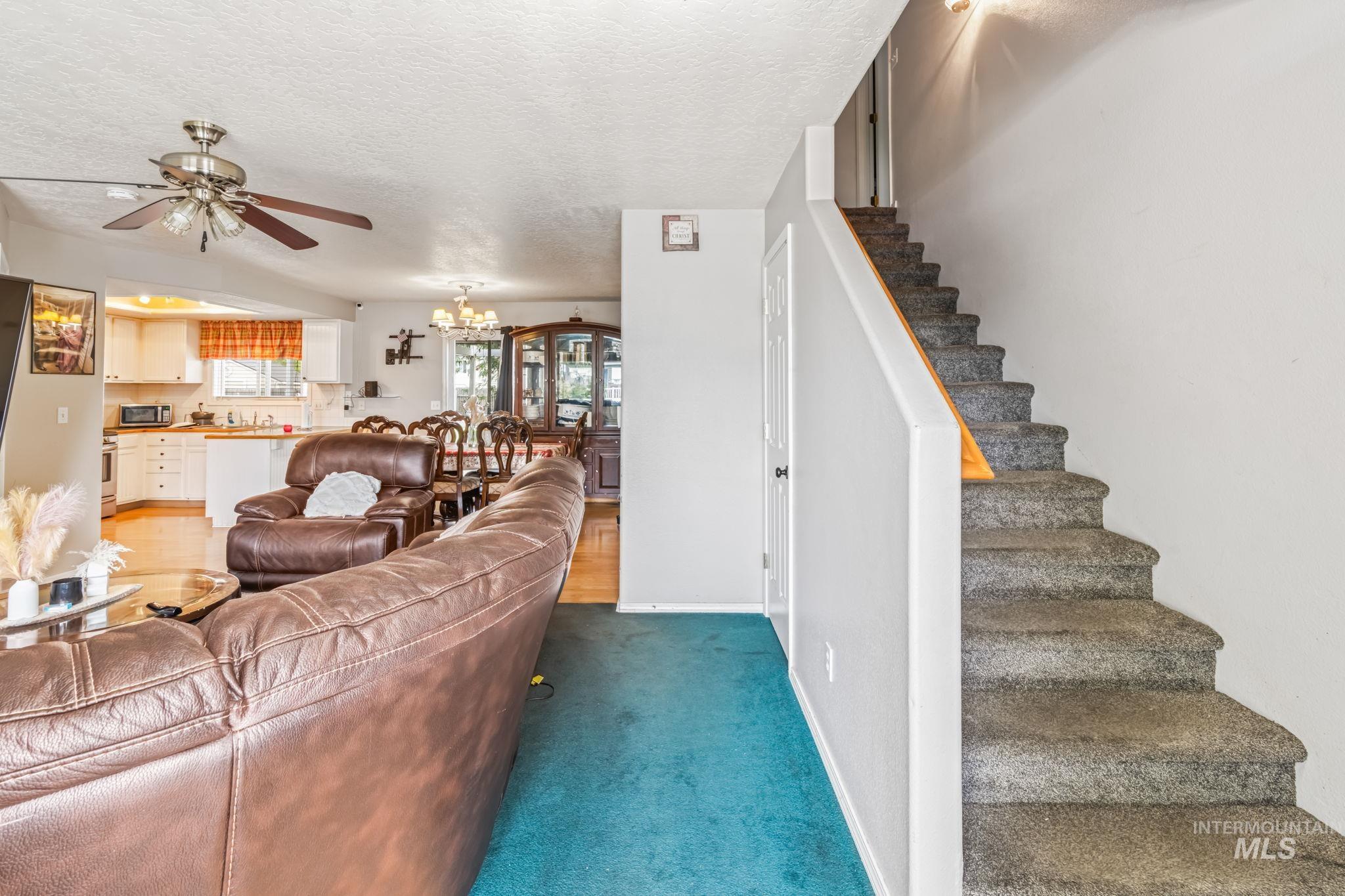 Living room with a chandelier, a textured ceiling, stairs, dark carpet, and a ceiling fan