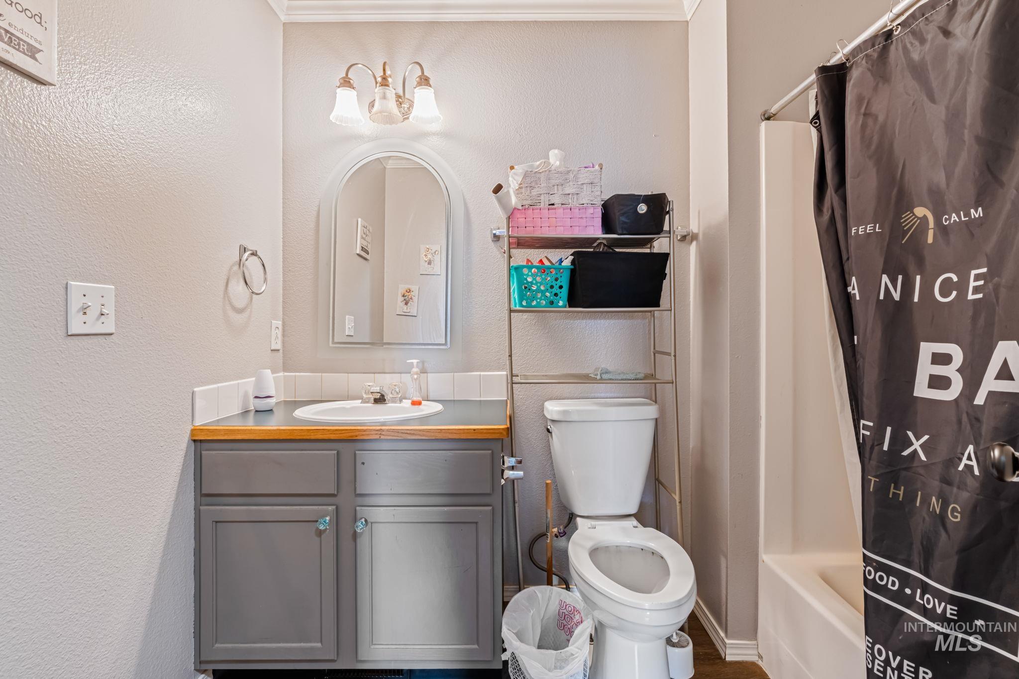 Full bath with vanity, shower / tub combo with curtain, a textured wall, and crown molding