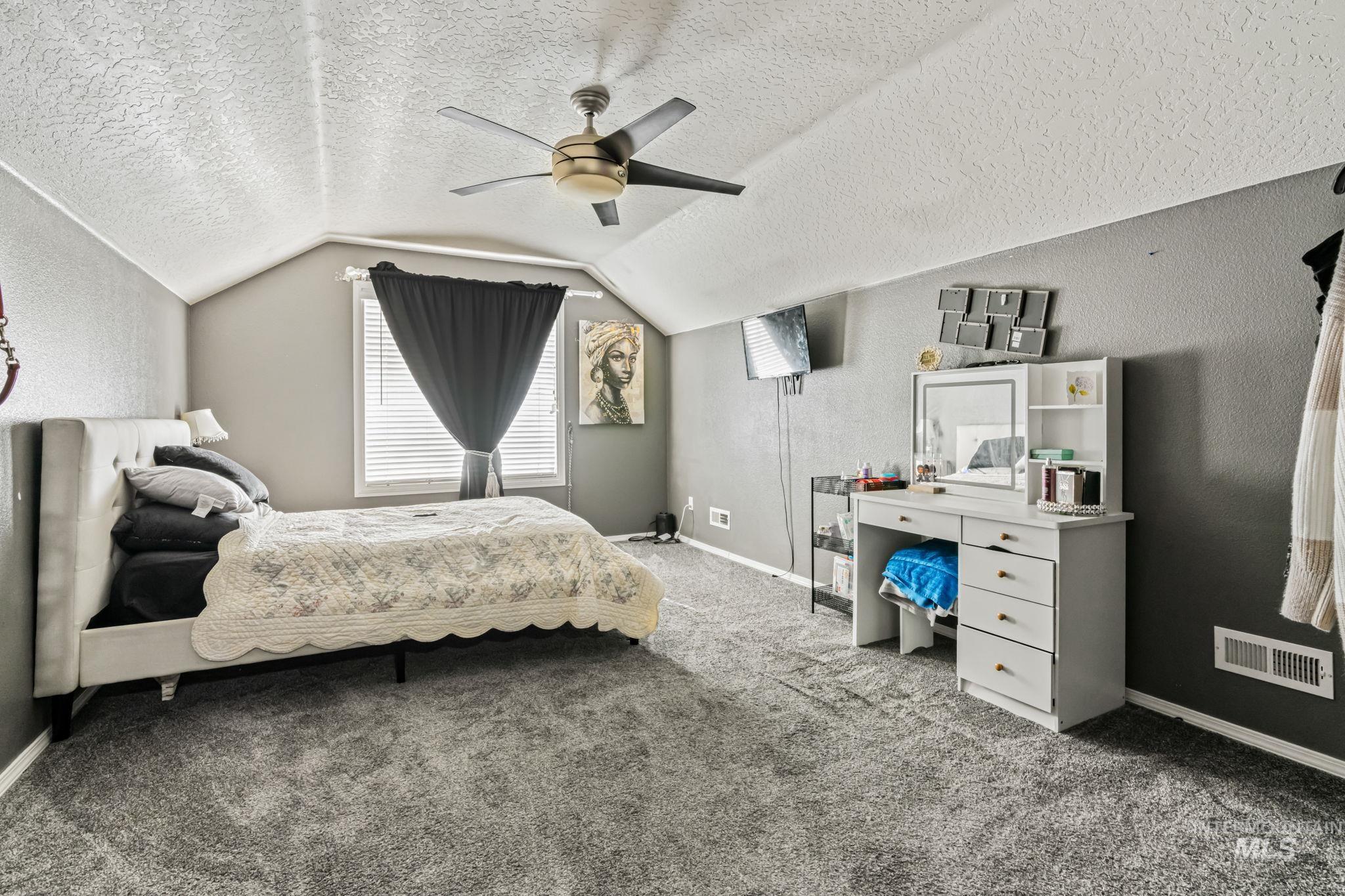 Bedroom featuring a textured wall, light carpet, a textured ceiling, vaulted ceiling, and ceiling fan