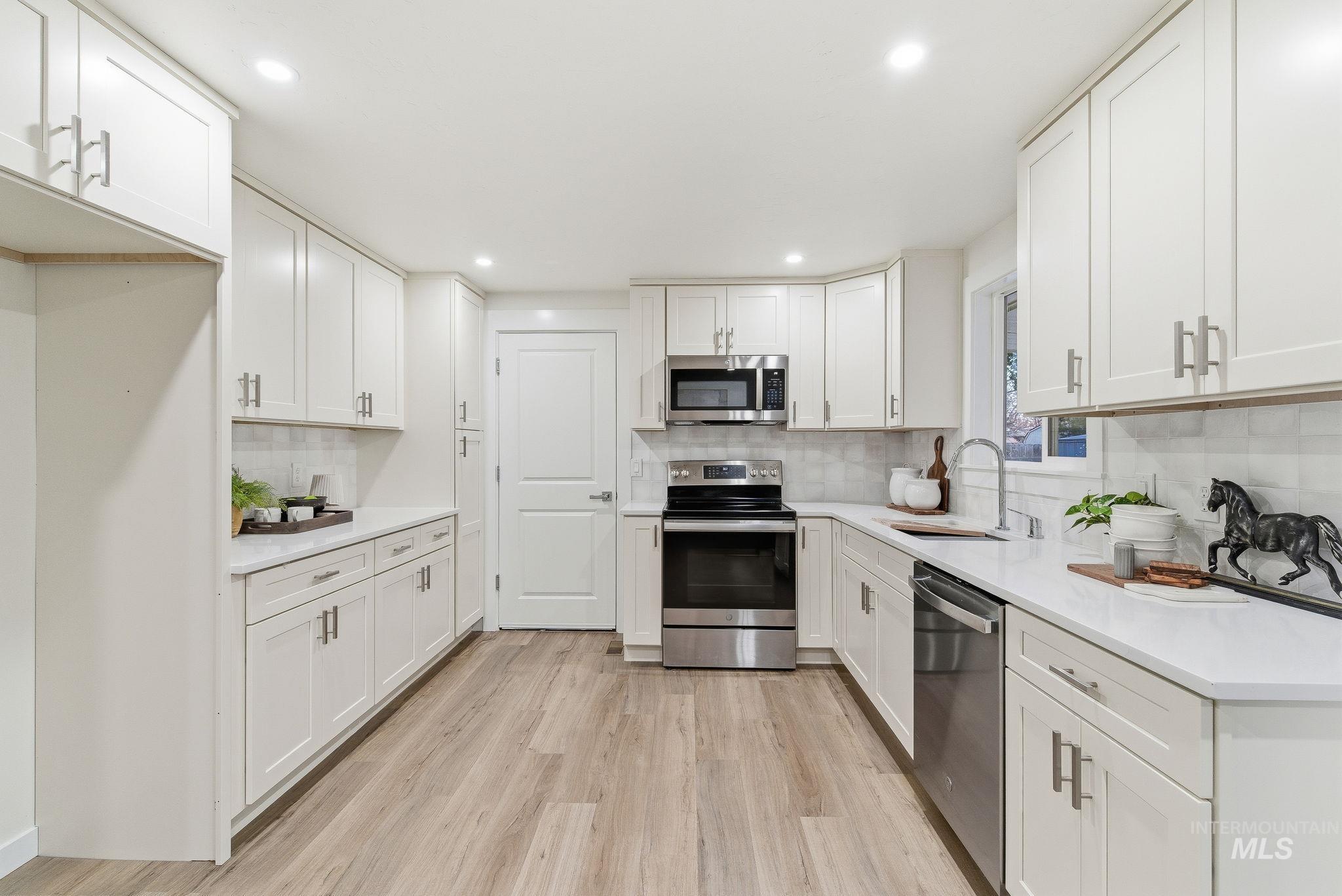 Kitchen featuring stainless steel appliances, white cabinets, light wood-style floors, tasteful backsplash, and recessed lighting