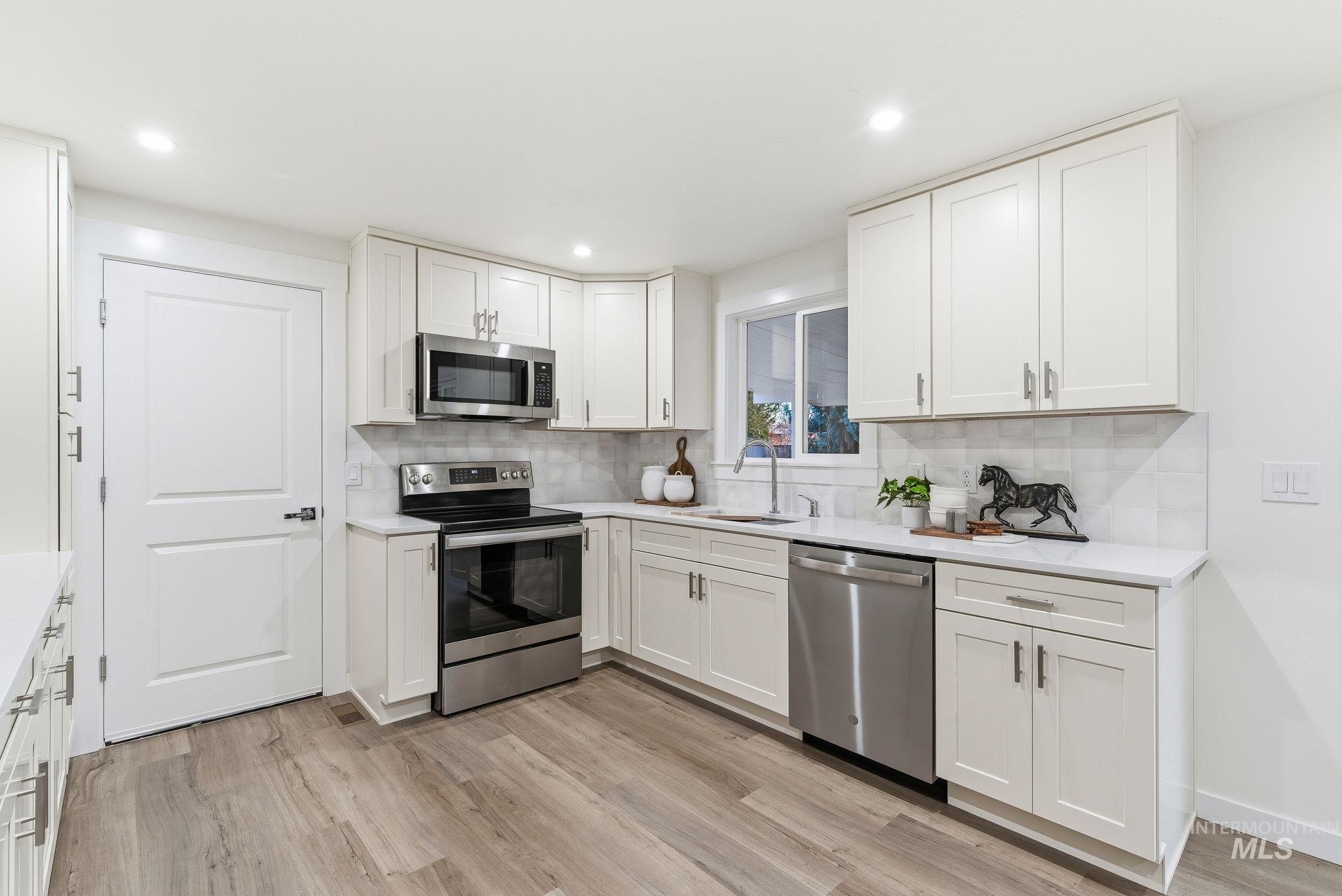 Kitchen with appliances with stainless steel finishes, white cabinets, backsplash, light wood-type flooring, and light stone countertops