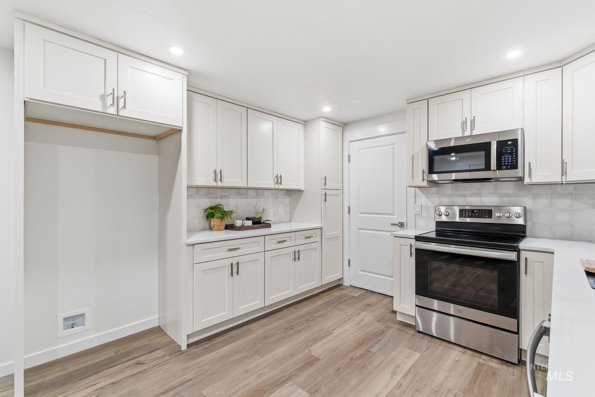 Kitchen featuring stainless steel appliances, white cabinets, light wood-type flooring, light stone counters, and recessed lighting