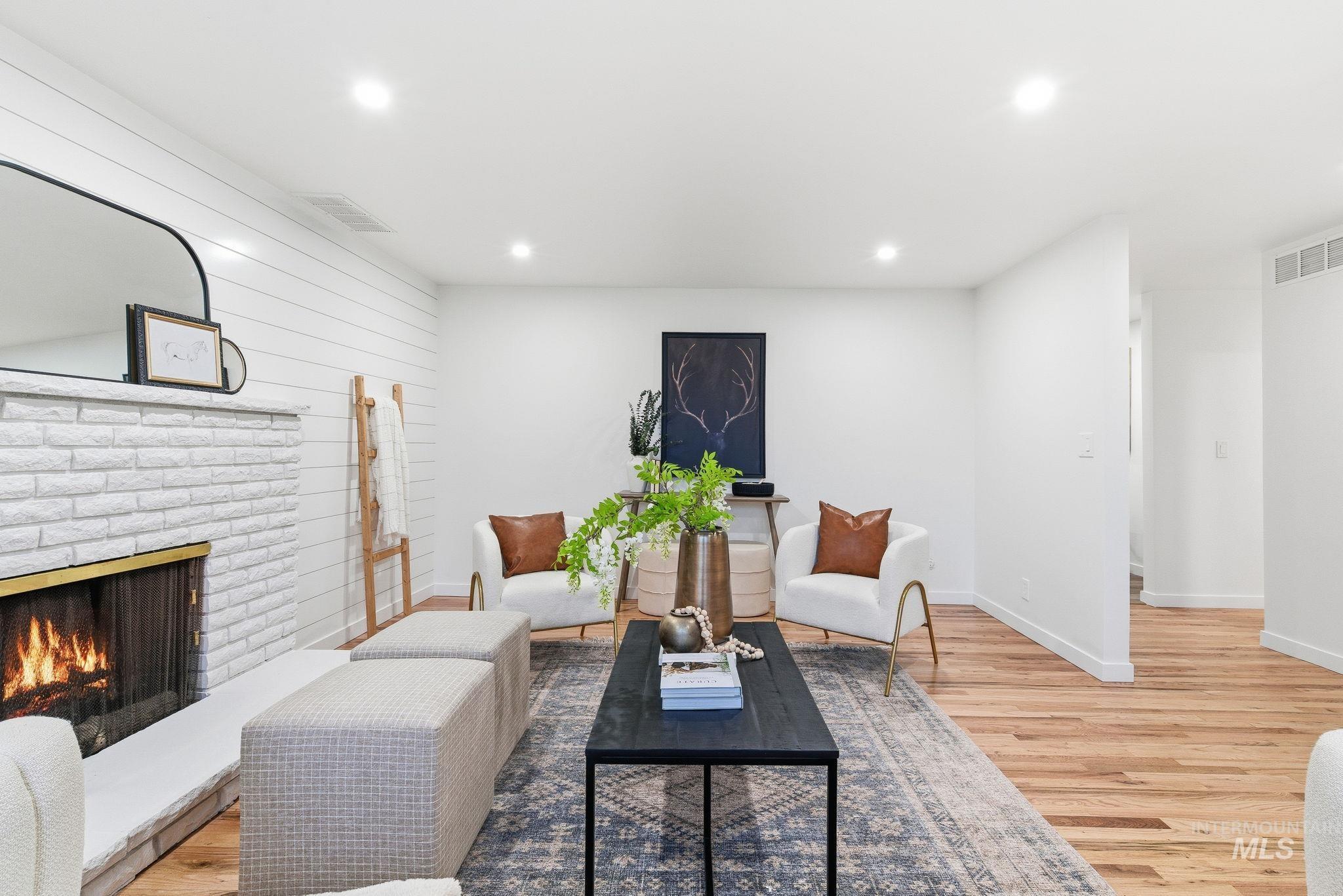 Living area with a brick fireplace, light wood finished floors, recessed lighting, and wood walls