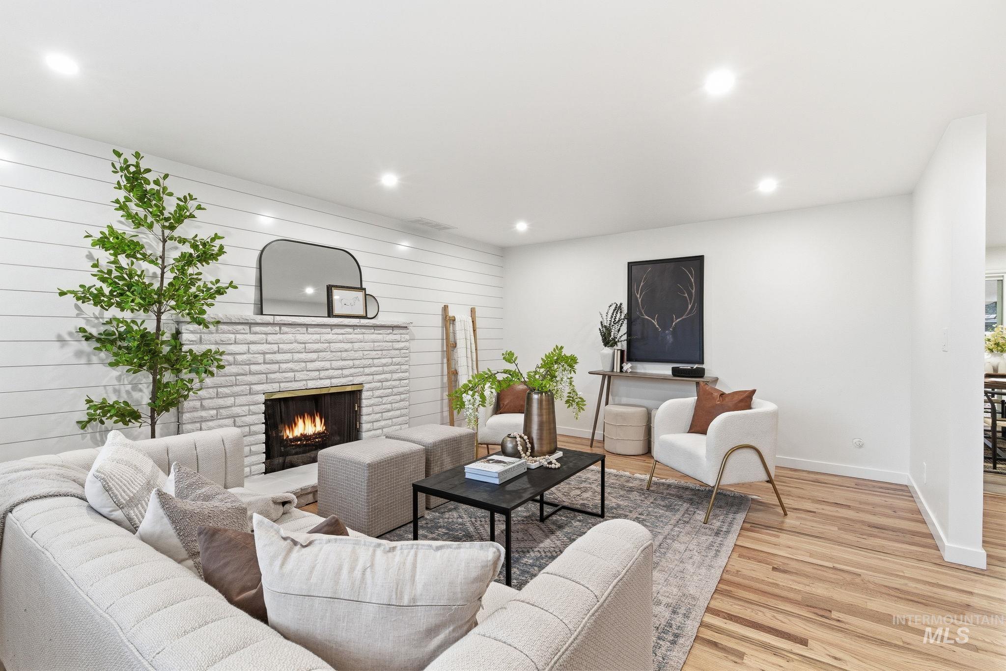 Living room with light wood finished floors, a brick fireplace, recessed lighting, and wood walls