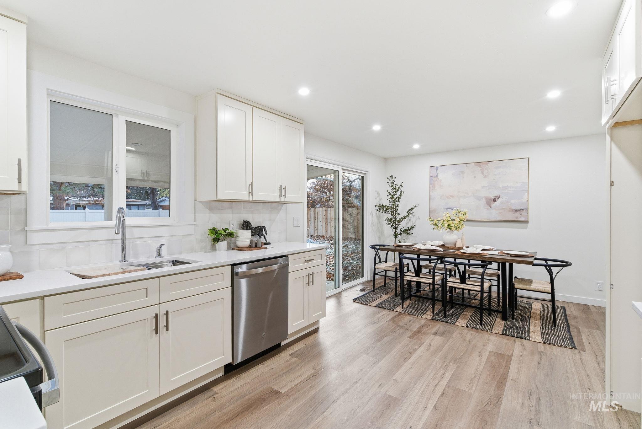 Kitchen with white cabinets, tasteful backsplash, stainless steel dishwasher, light wood-style floors, and light stone countertops