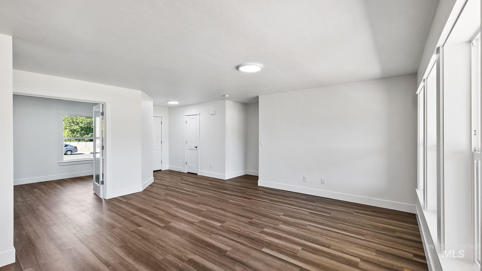 Unfurnished living room featuring dark wood-style flooring and baseboards