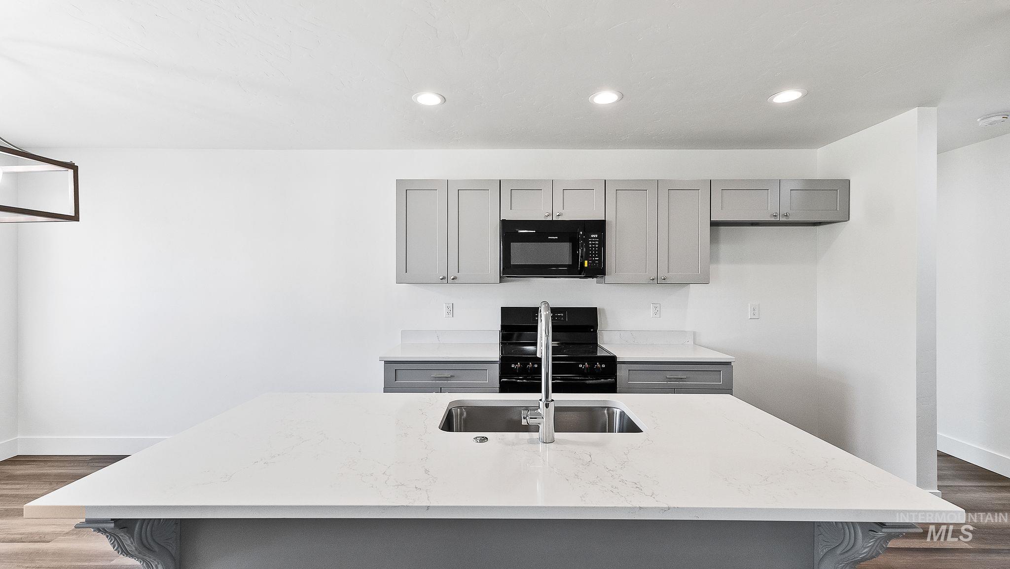 Kitchen with gray cabinetry, dark wood finished floors, black appliances, light stone countertops, and recessed lighting