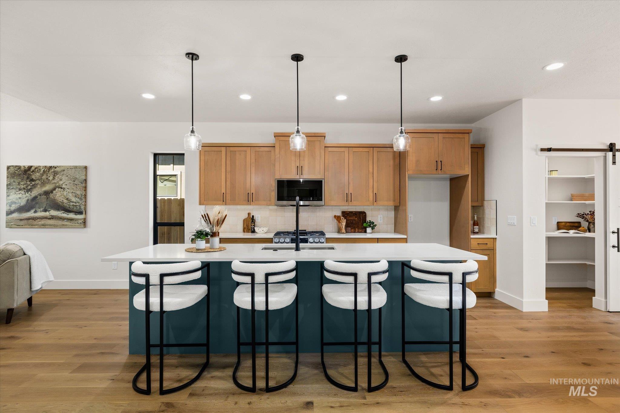 Kitchen featuring a barn door, backsplash, light countertops, a kitchen island with sink, and recessed lighting