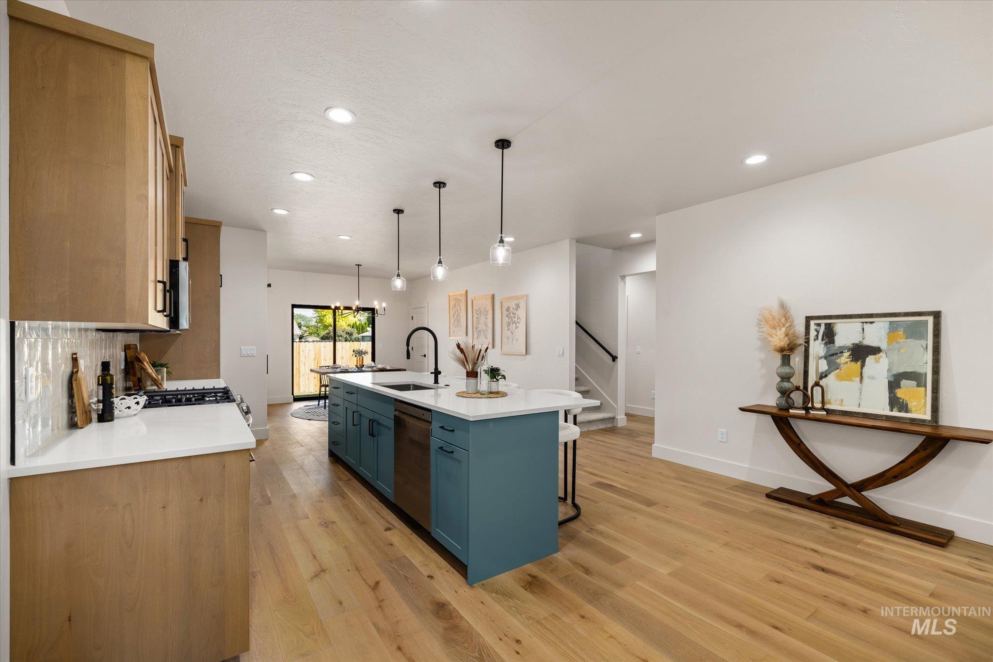 Kitchen featuring light wood-style flooring, light countertops, recessed lighting, a kitchen island with sink, and decorative light fixtures