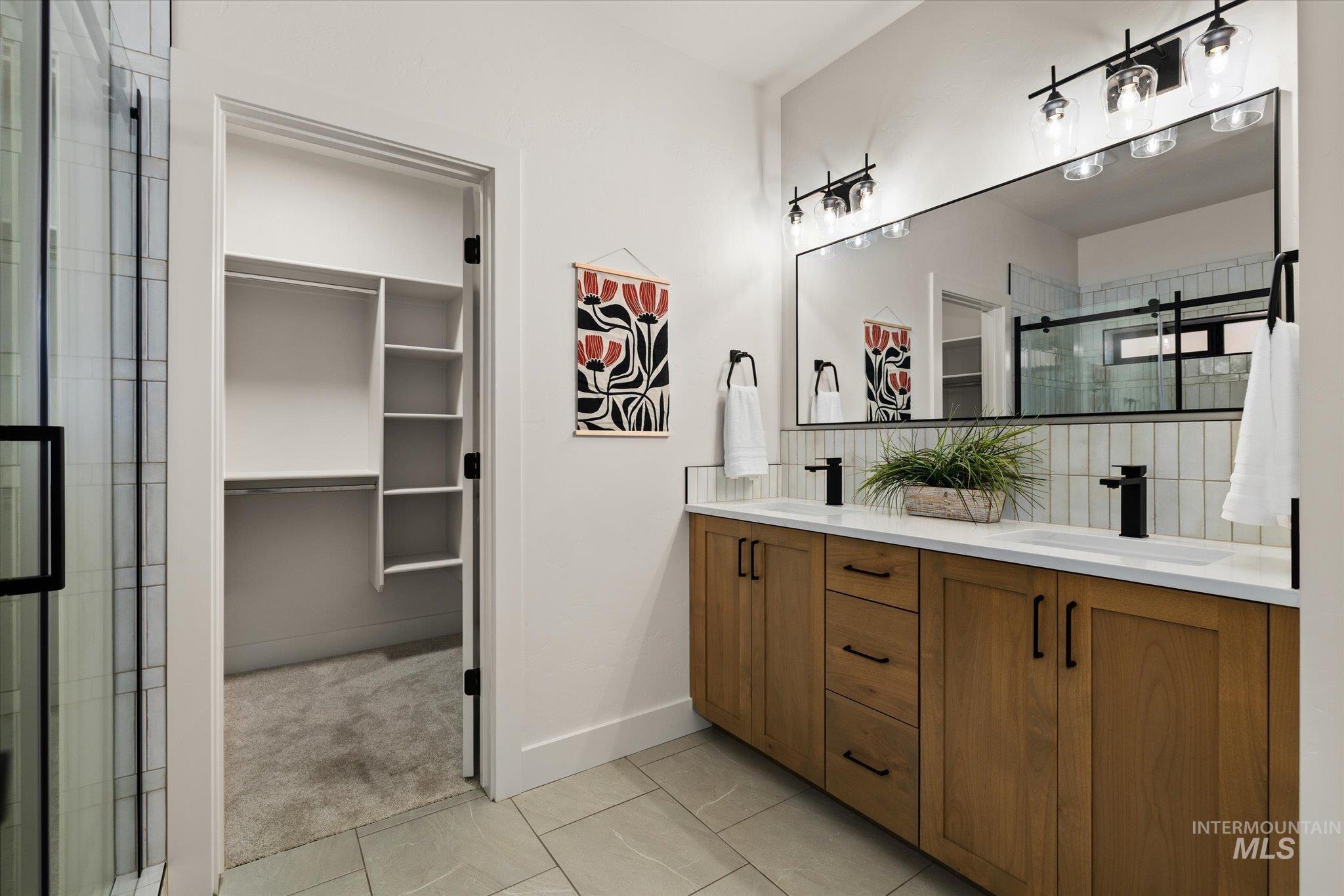 Bathroom featuring a walk in closet, double vanity, tile patterned floors, and a shower stall
