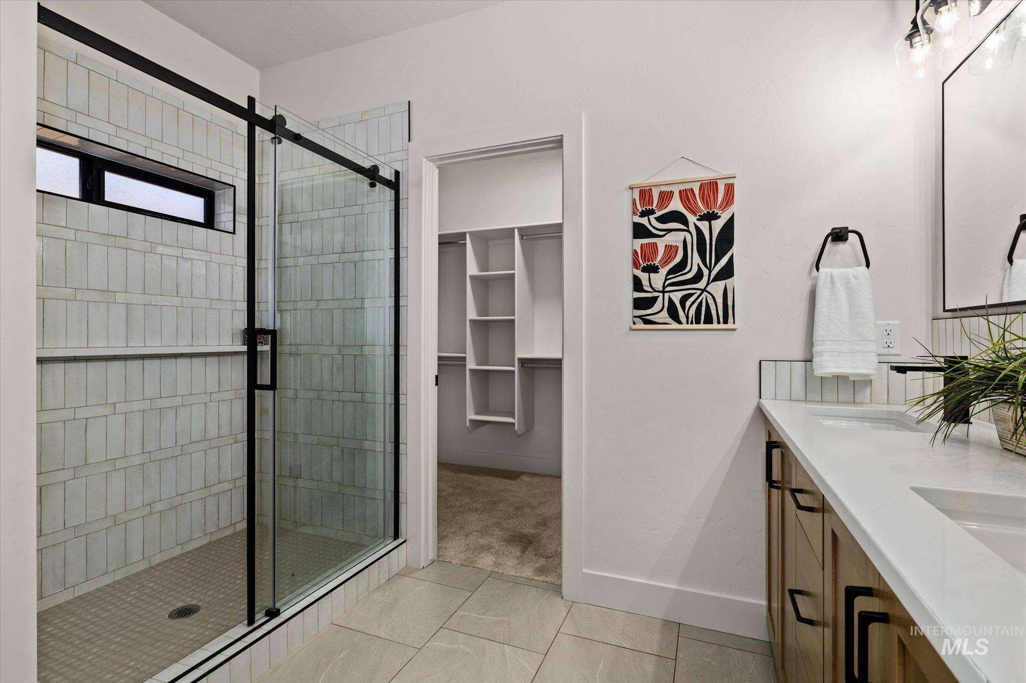 Full bathroom featuring tile patterned flooring, a stall shower, double vanity, and a spacious closet