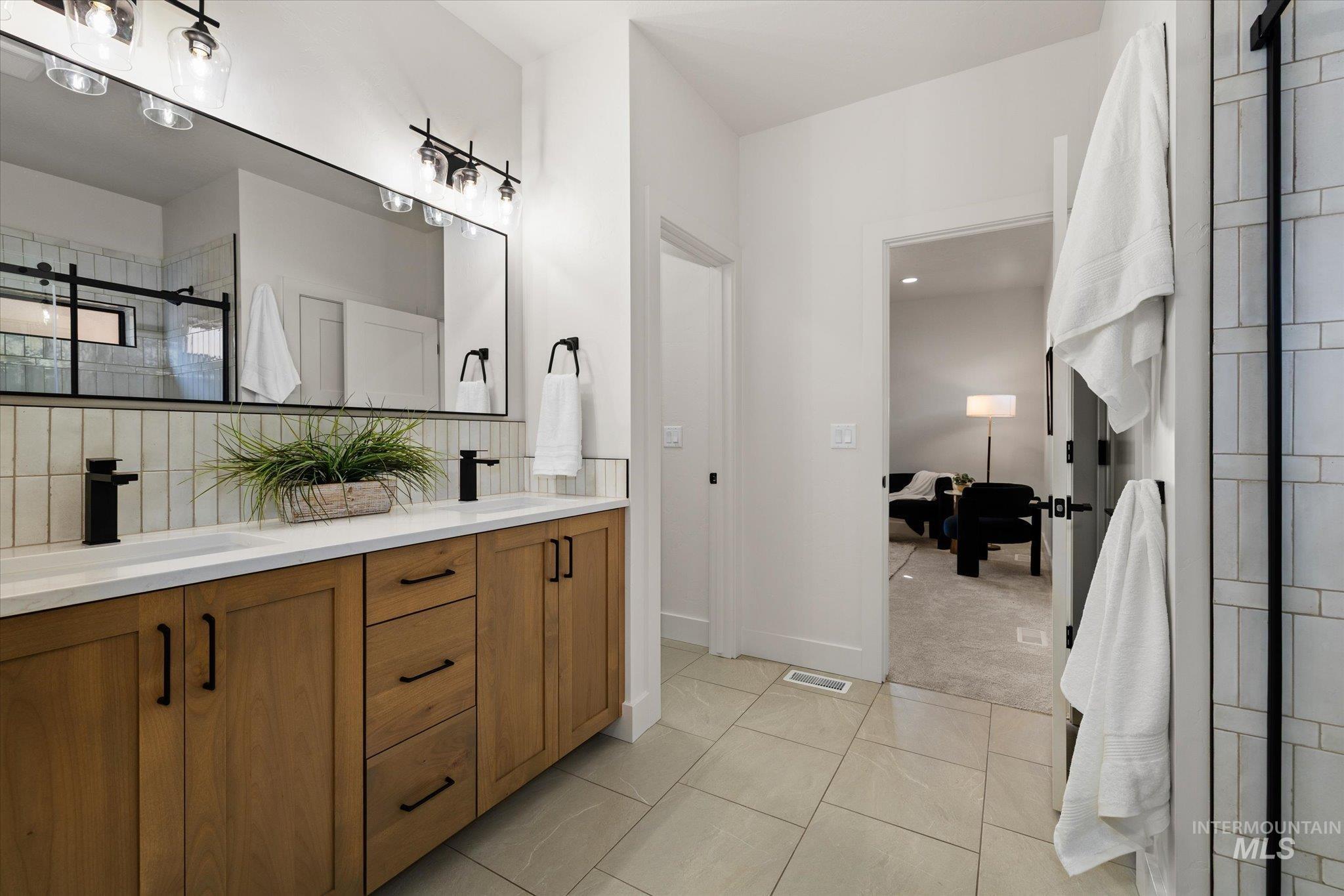 Full bathroom featuring double vanity, tile patterned flooring, a shower stall, and decorative backsplash