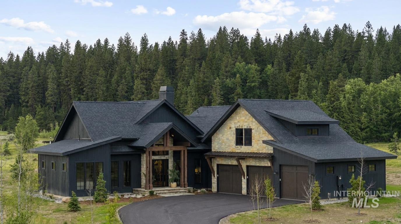 View of front of property with stone siding, board and batten siding, driveway, a view of trees, and an attached garage - sitting on .55 acres.