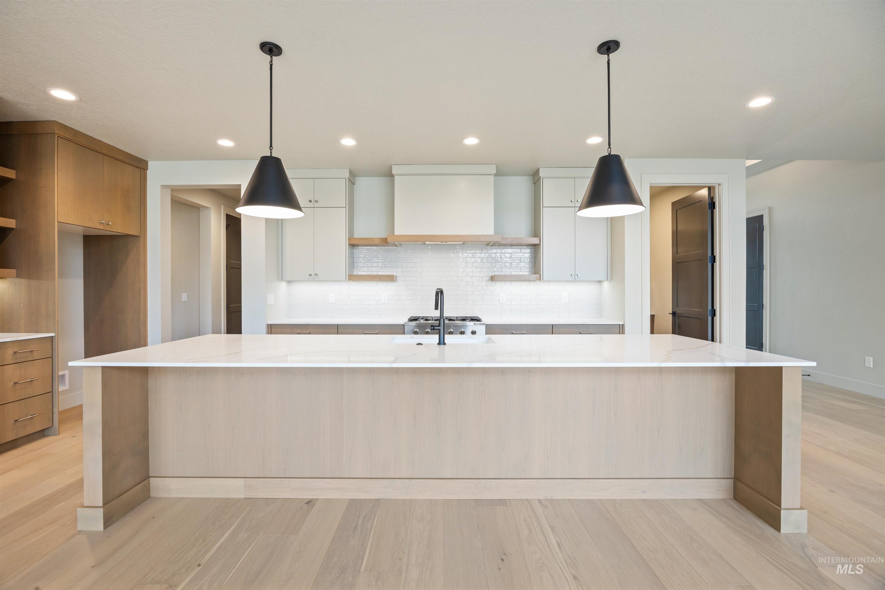 Dual tone kitchen featuring open shelves, hanging light fixtures, a large island, light stone countertops, and decorative backsplash