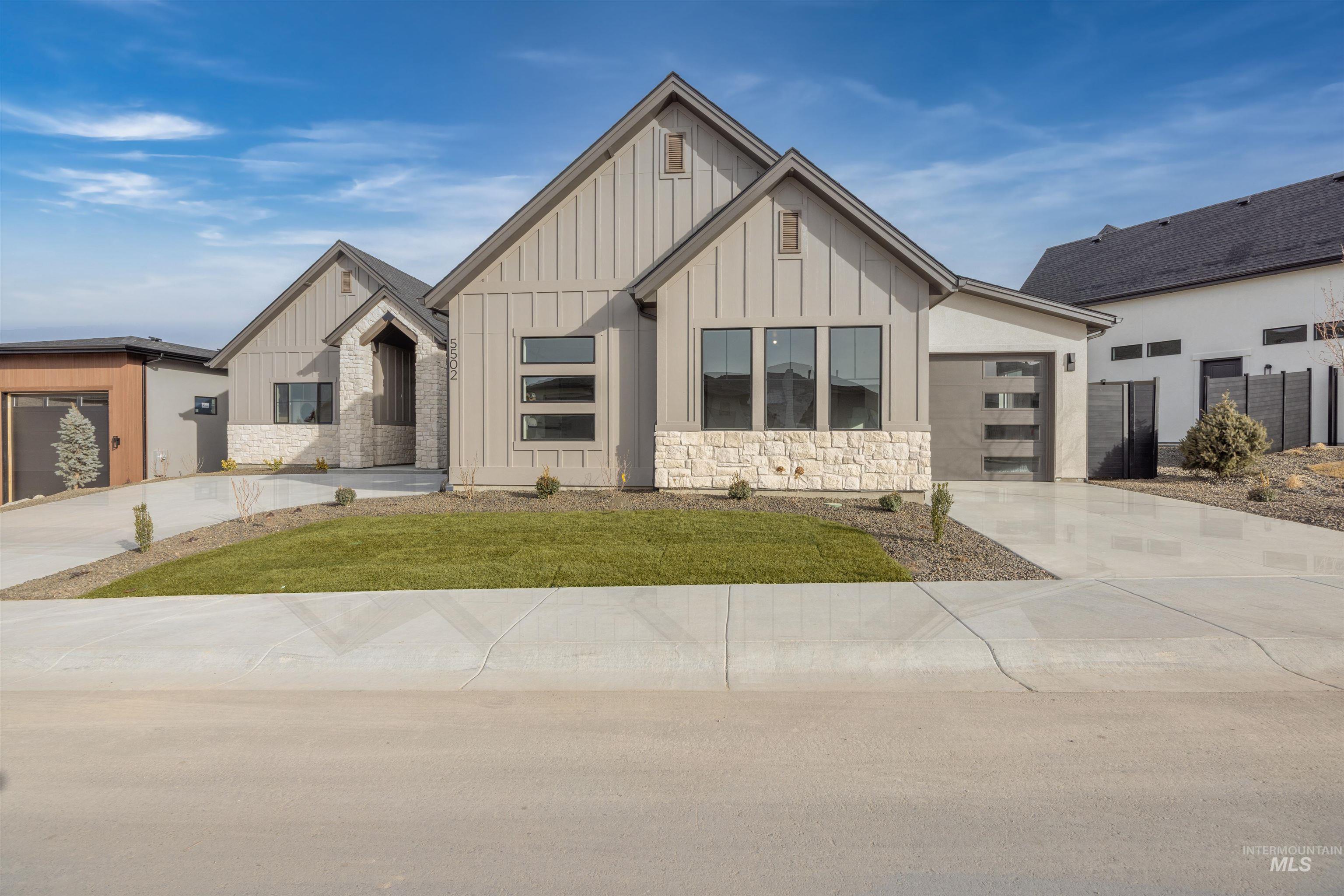 Modern inspired farmhouse featuring board and batten siding, stone siding, driveway, and a front yard