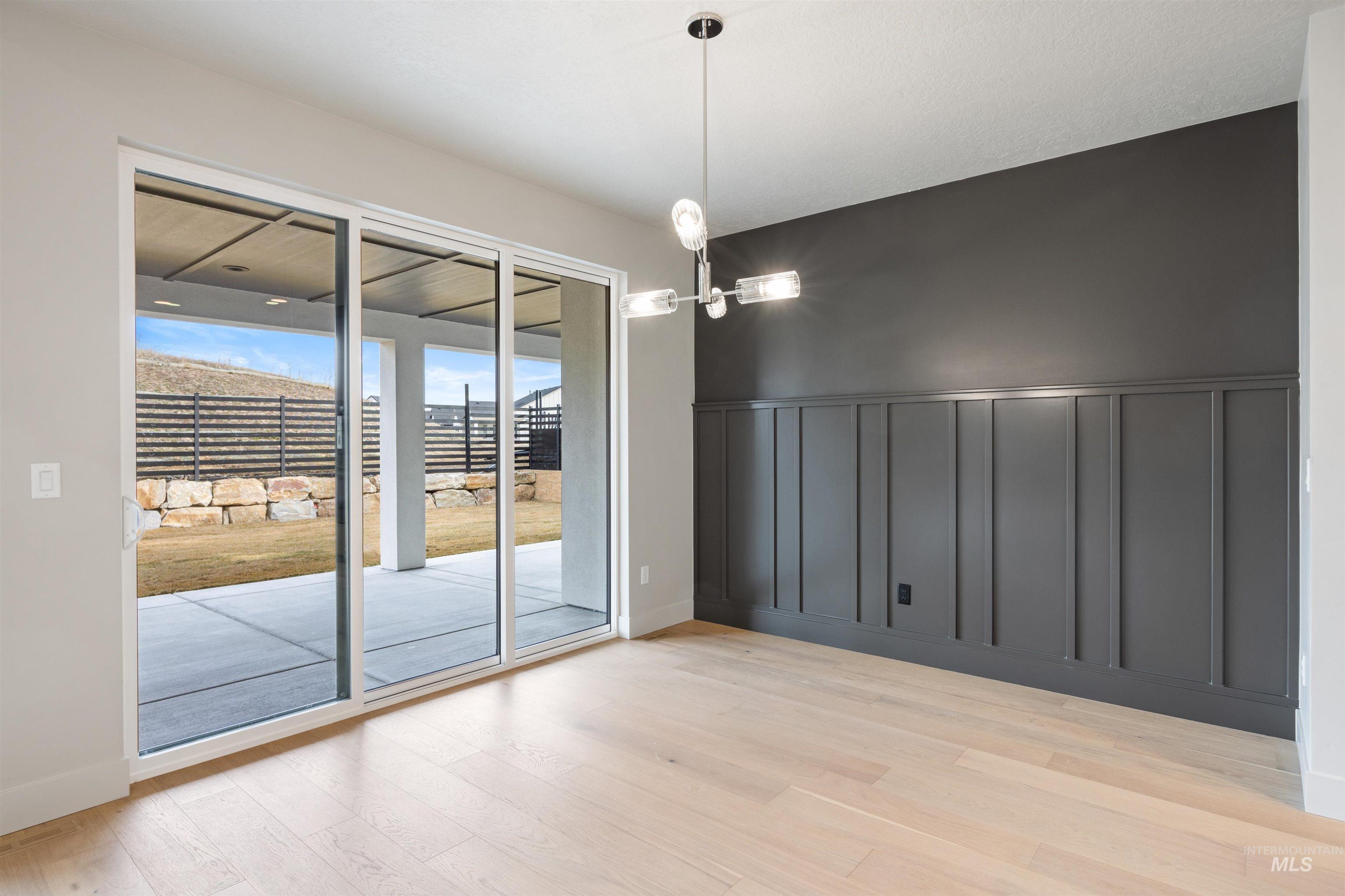 Spare room with light wood-style floors, suspended lighting, and wainscoting