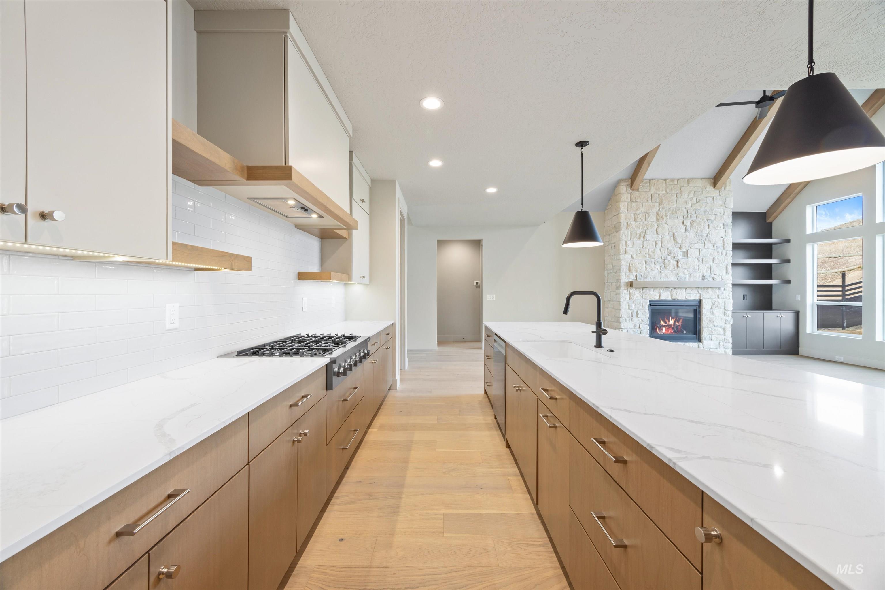 Dual tone kitchen with a stone fireplace, light wood finished floors, light stone counters, open shelves, and pendant lighting