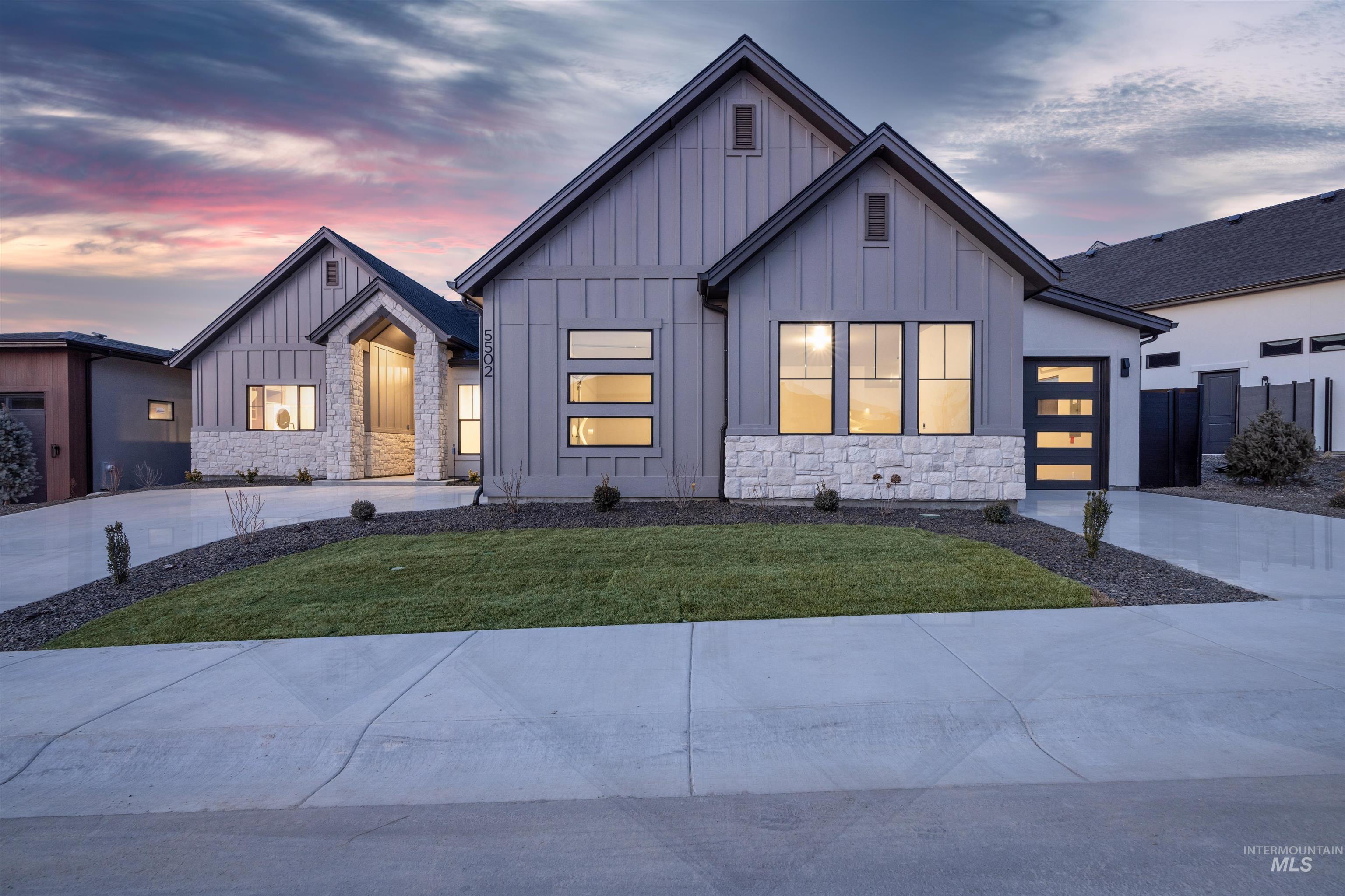 Modern inspired farmhouse with stone siding, board and batten siding, a lawn, and driveway