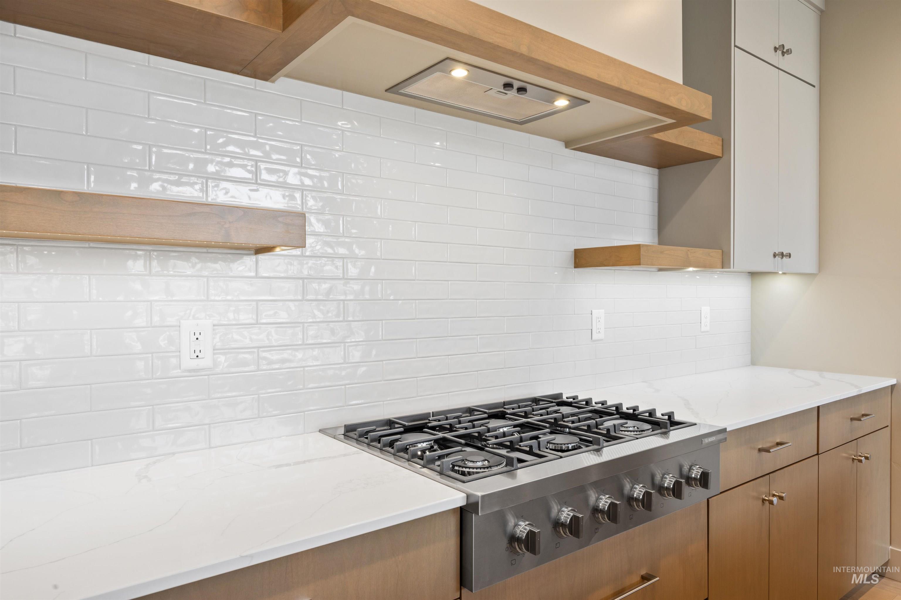 Kitchen with open shelves, stainless steel gas cooktop, light stone countertops, and backsplash
