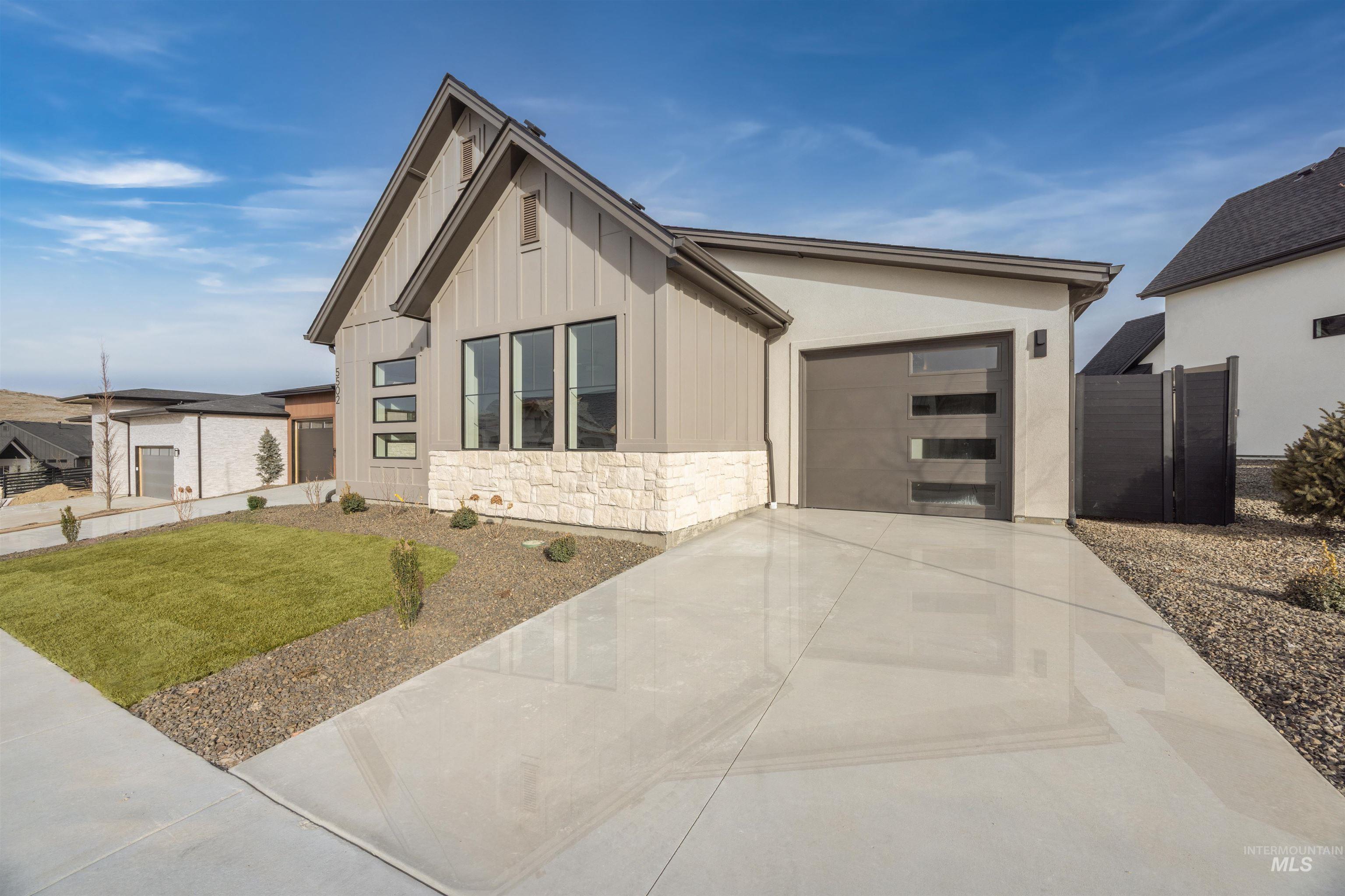 View of front facade with stone siding, driveway, a garage, and board and batten siding