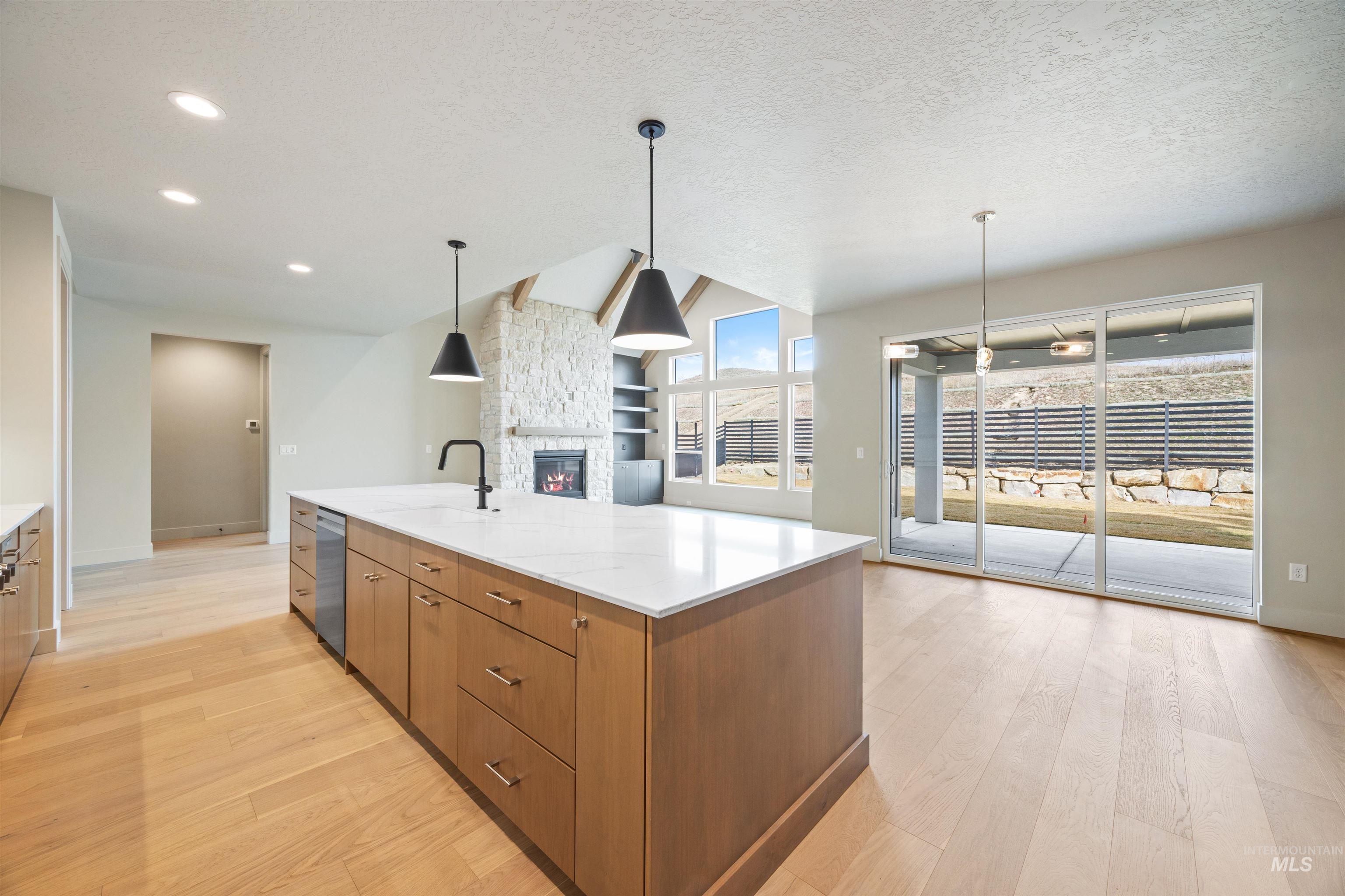 Kitchen featuring wood finish cabinets, a large island, hanging light fixtures, a stone fireplace, and a textured ceiling