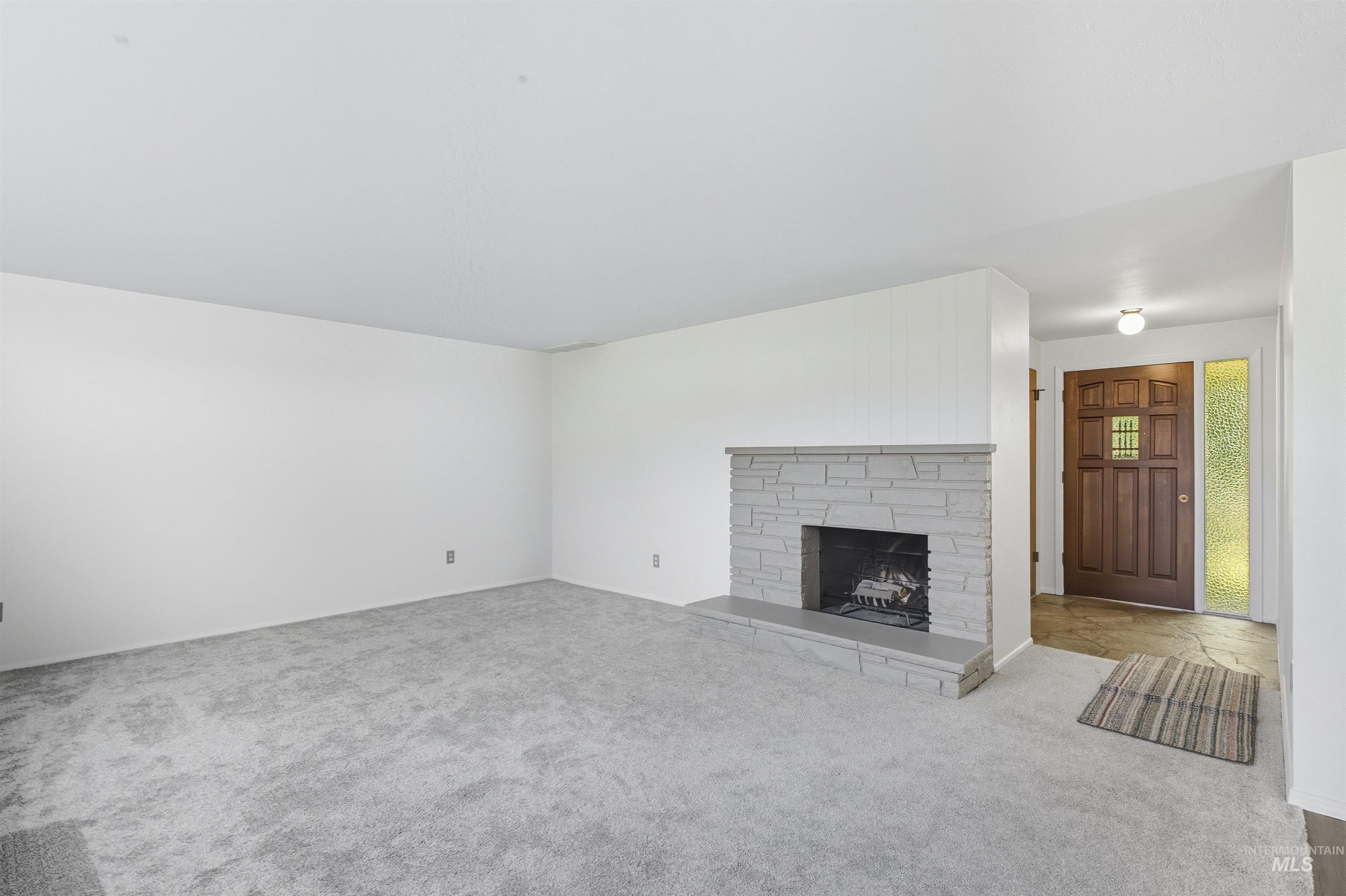 Unfurnished living room featuring carpet floors and a fireplace with raised hearth